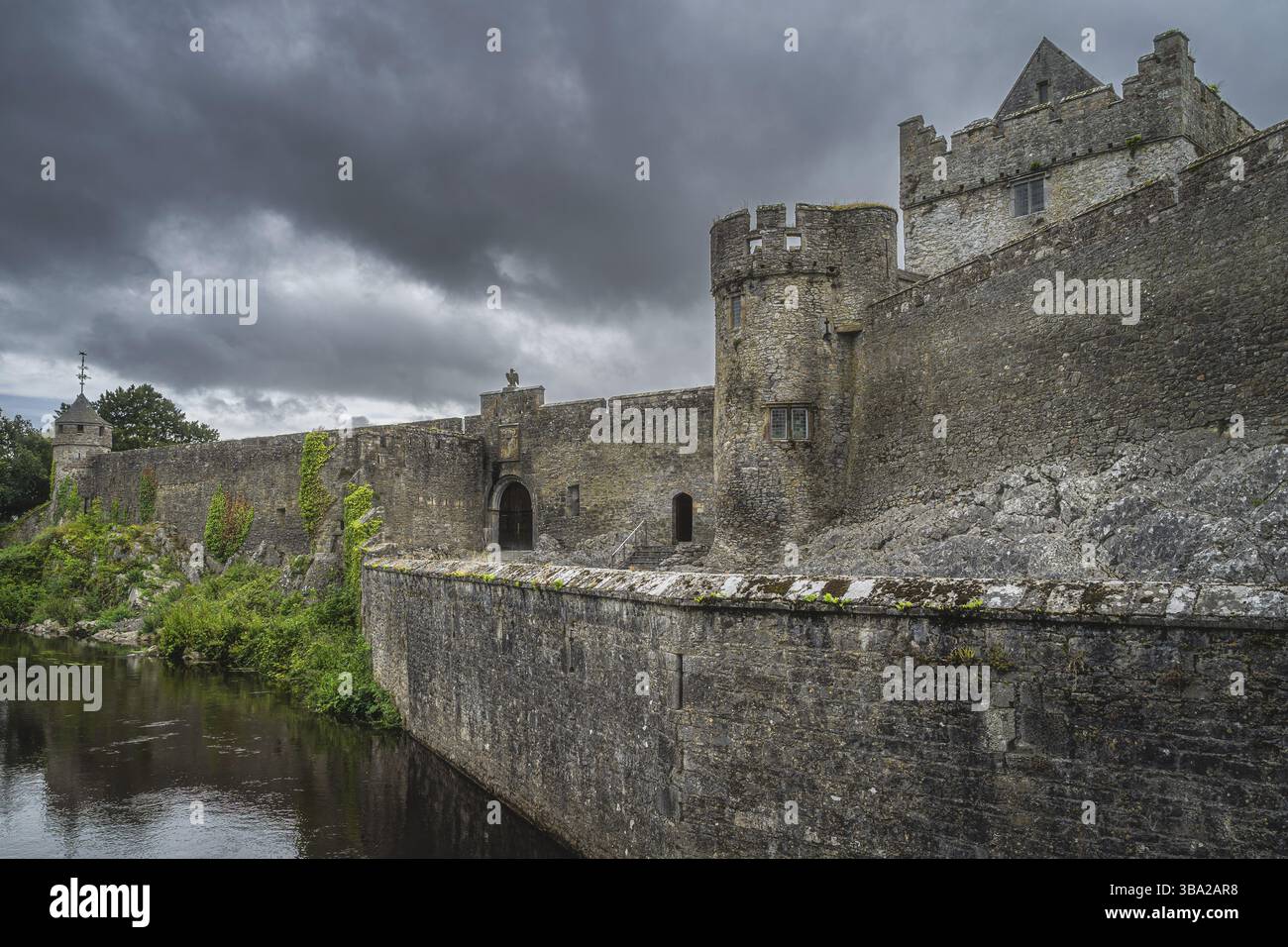 Hohe Steinmauern und Wassergraben der Cahir-Burg aus dem 11. Jahrhundert in Cahir-Stadt mit dramatischem Sturmhimmel im Hintergrund, County Tipperary, Irland, Europa Stockfoto