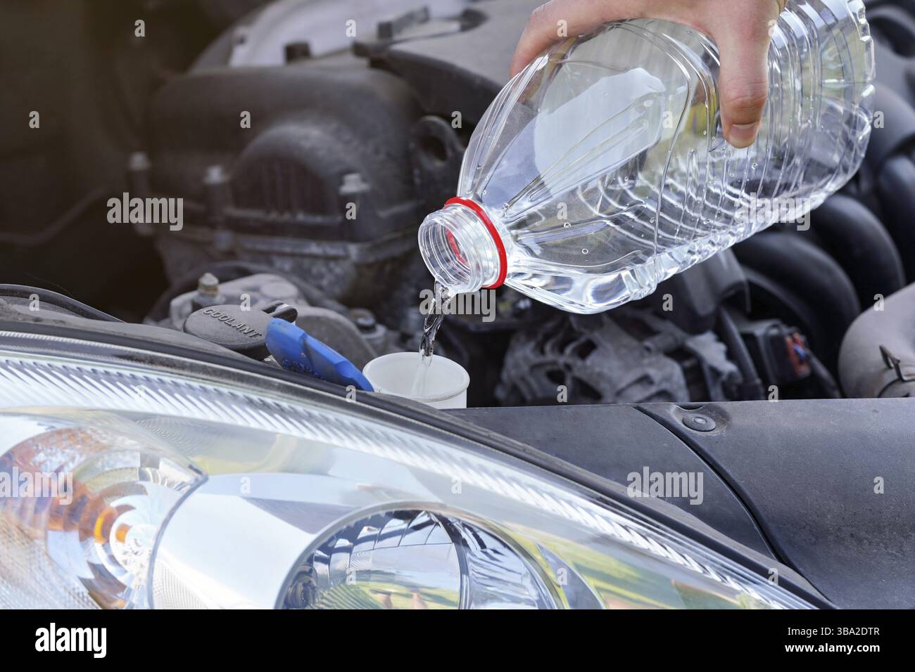 Mann gießt destilliertes Wasser (ökologische Alternative zu Waschflüssigkeit) in den Waschtank im Auto, Detail auf der Hand hält klare Plastikflasche, Liptovsky Mi Stockfoto