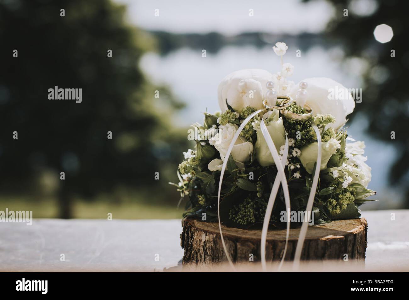 Hochzeitsstrauß mit weißen Rosen und Ringen, die an sonnigen Tagen draußen angebracht werden Stockfoto