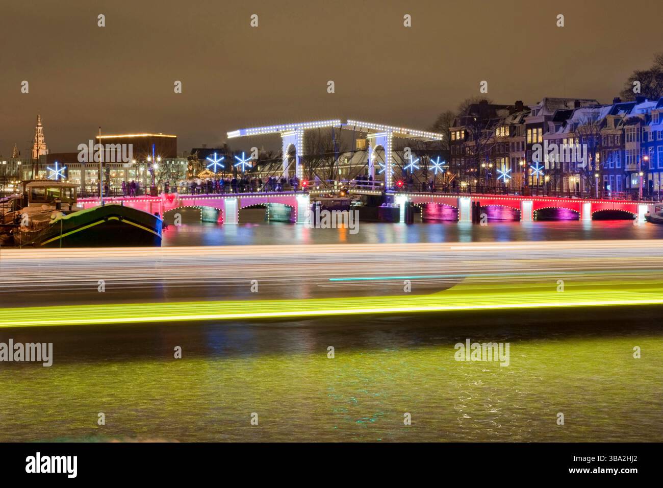 Magere Brug Amsterdam, während der Weihnachts-Kanalparade. Leichte Wege vorbeifahrender Boote. Stockfoto