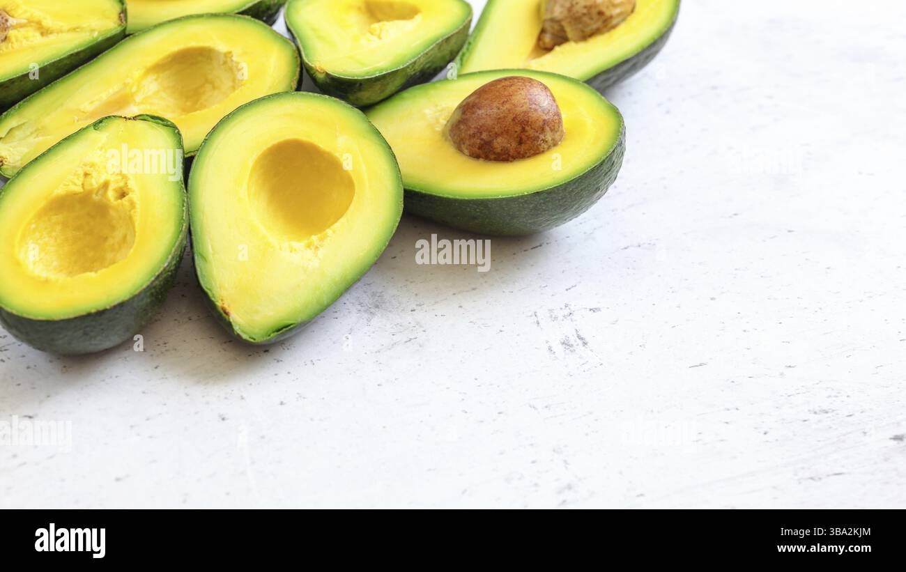 Halbierte Avocadofrüchte mit grünem gelbem Fruchtfleisch, einige braune Samen sichtbar auf weißem Arbeitsbrett - Platz für Text rechts, Liptovsky Hradok, Slowakei, Euro Stockfoto