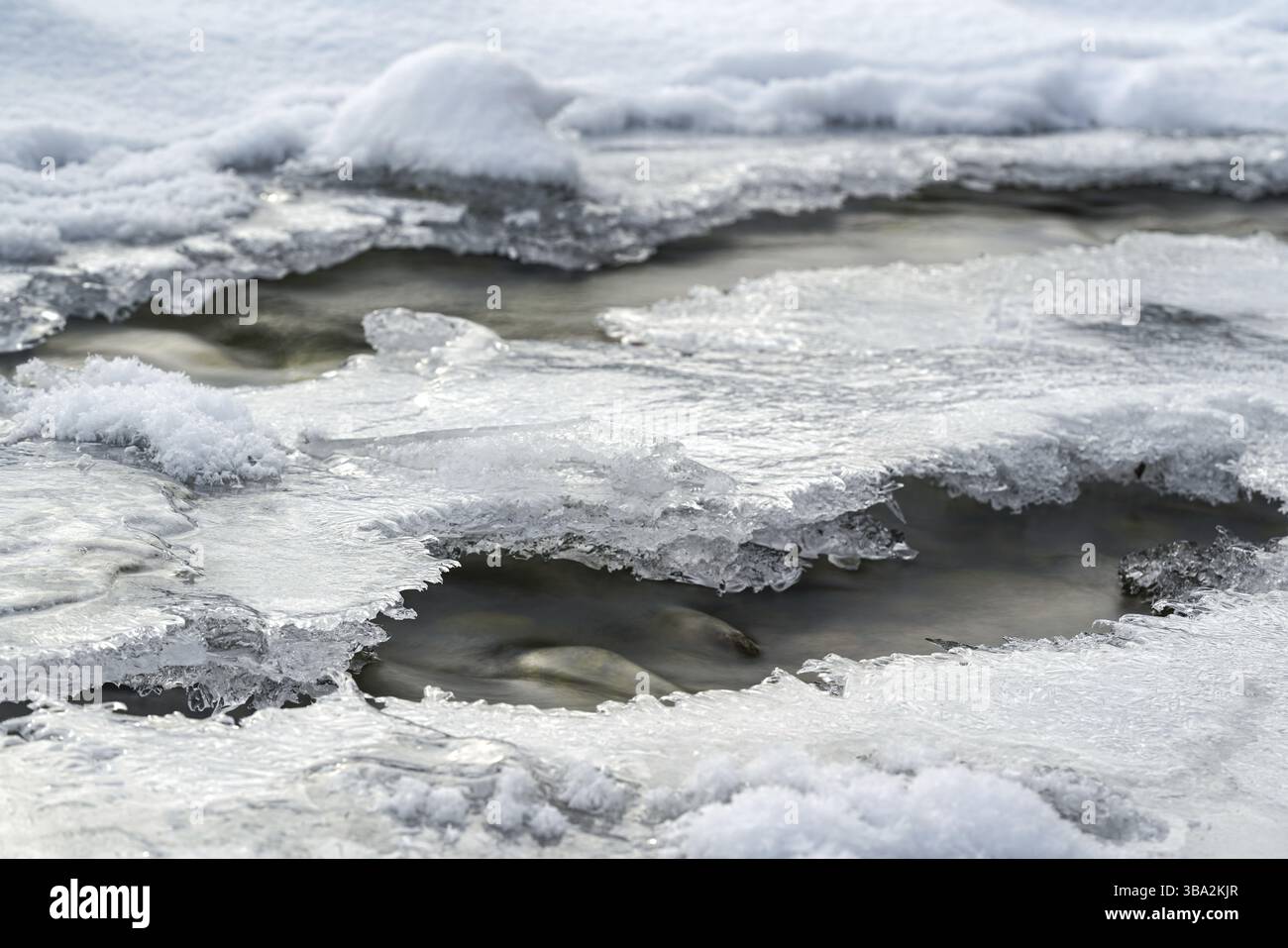 Flachwald Fluss mit Kristallschnee und Eisschicht im Winter bedeckt, weisse Flecken ueber Steine, lange Exposition Foto Stockfoto