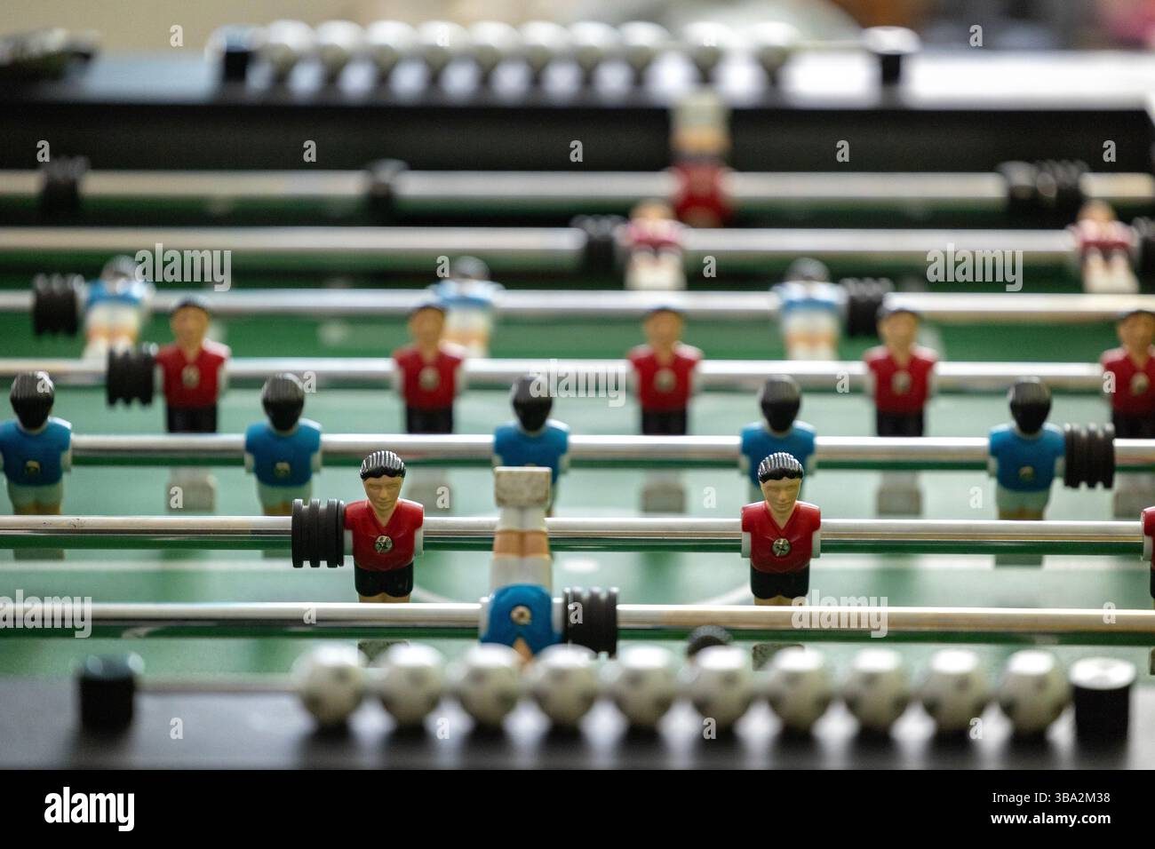 Ein Tischkicker mit roten und blauen Spielfiguren, die auf Metallstangen montiert sind. Die Spielfläche ist grün und schwarze Griffe dienen der Kontrolle. Die Abbildung Stockfoto