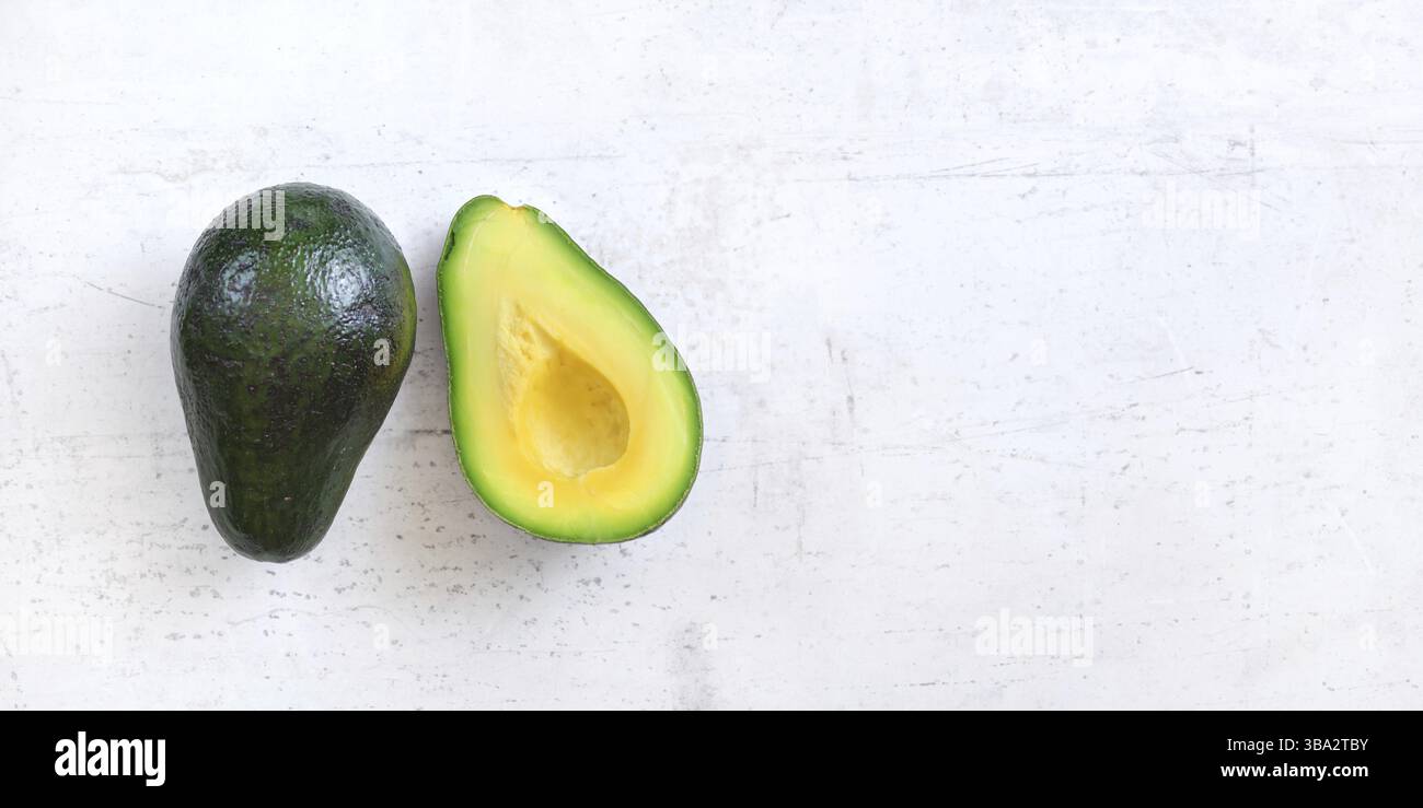 Überkopfaufnahme – Avocados, einer in zwei Hälften auf weißem Arbeitsbrett. Breites Banner mit Platz für Text rechts, Liptovsky Hradok, Slowakei, Europa Stockfoto
