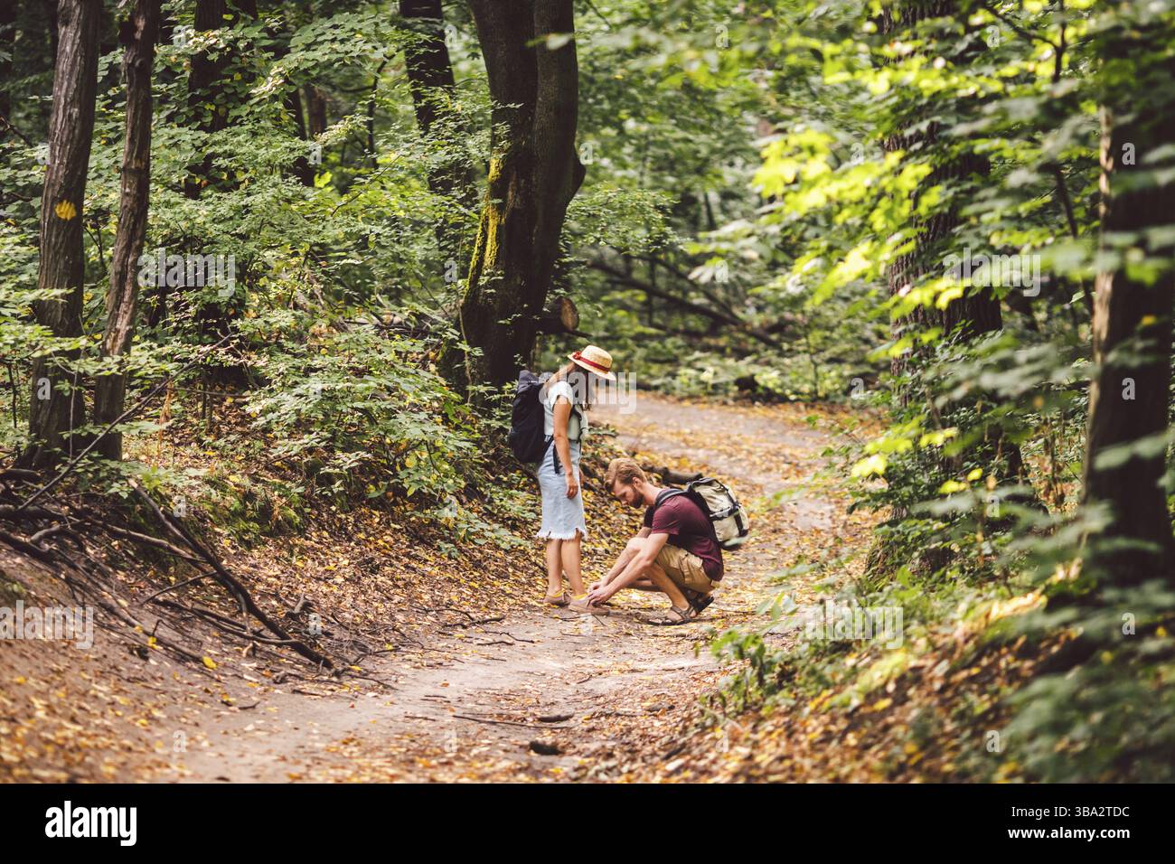 Hipster-Paar Wanderer hält an, um ihren Schuh auf Sommer-Wanderweg im Wald zu binden. Mann, Der Frauen Schuhe Bindet. Spaß aktiven Lebensstil im Freien. Camper binden Schuh Stockfoto