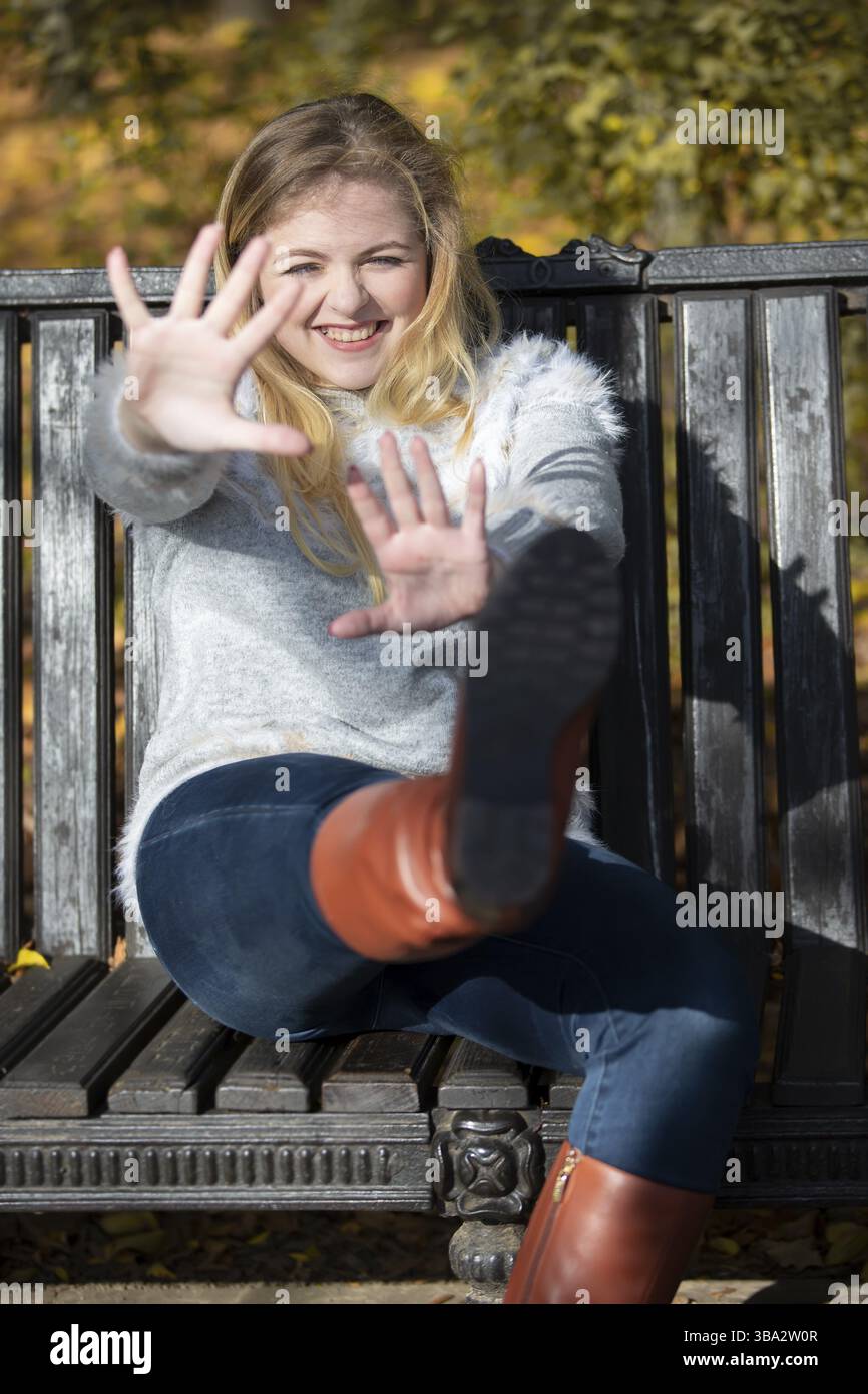 Schöne junge Frau in einem Herbstpark sitzt auf einer Bank Stockfoto