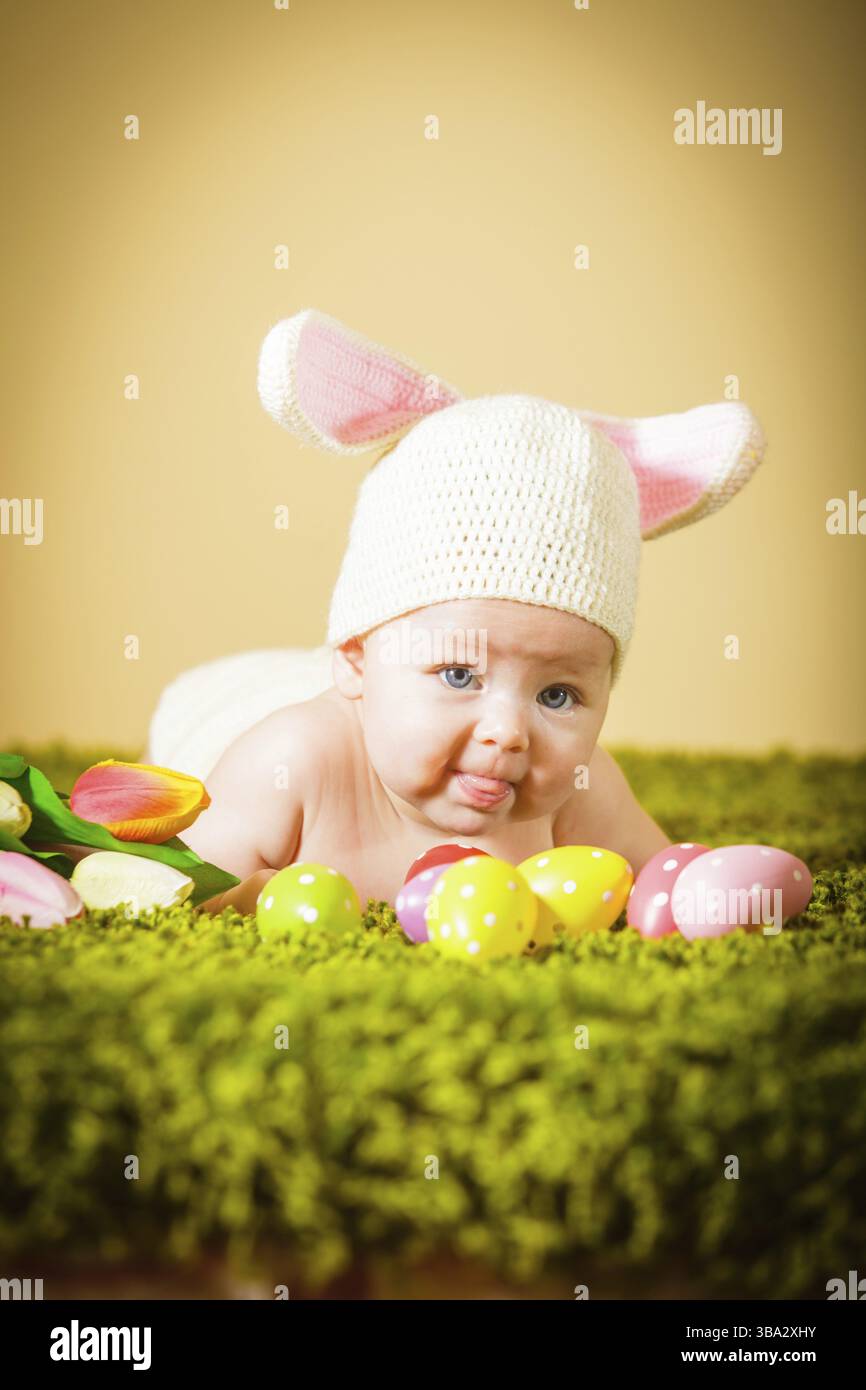 Drei Monate lang lag das Baby auf dem Bauch als Osterhase auf dem Gras mit Eiern Stockfoto