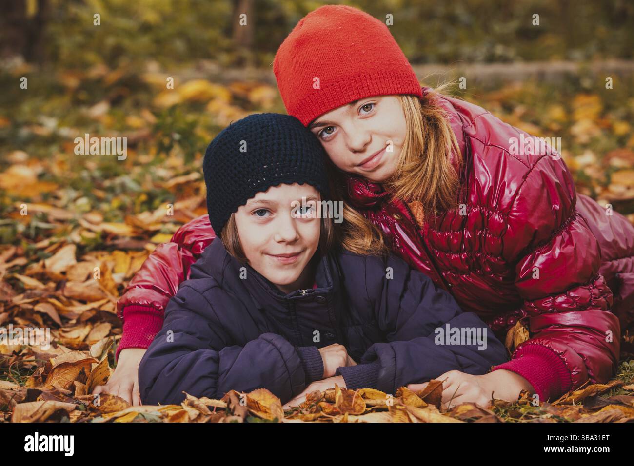 Zwei freundliche Schwestern, die mit Herbstblättern spielen und lächeln Stockfoto