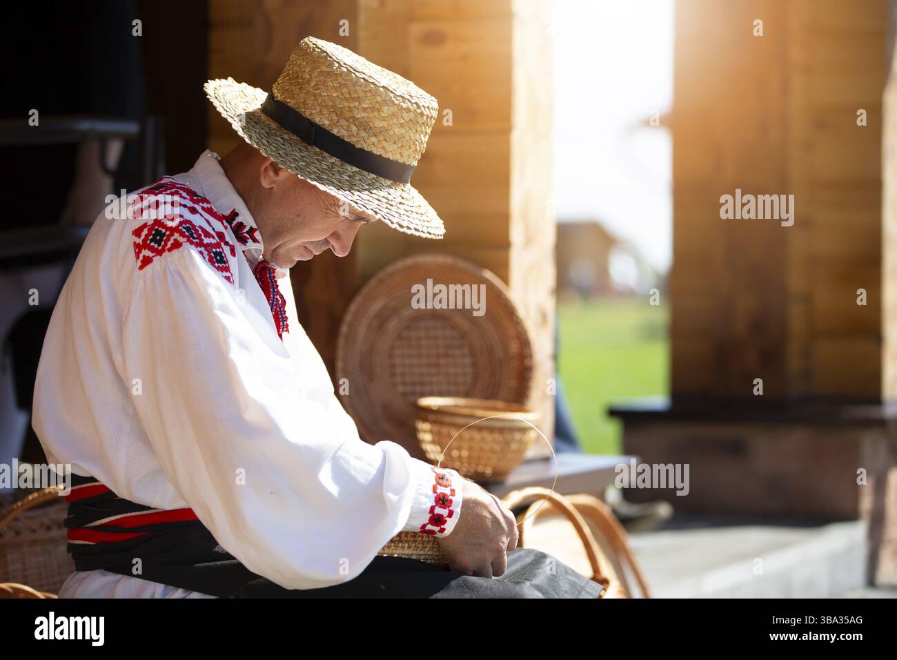 Ein Ukrinski oder weißrussischer Handwerker in besticktem Hemd webt Körbe aus Birkenrinde. Der Mann macht Birkenkörbe Stockfoto