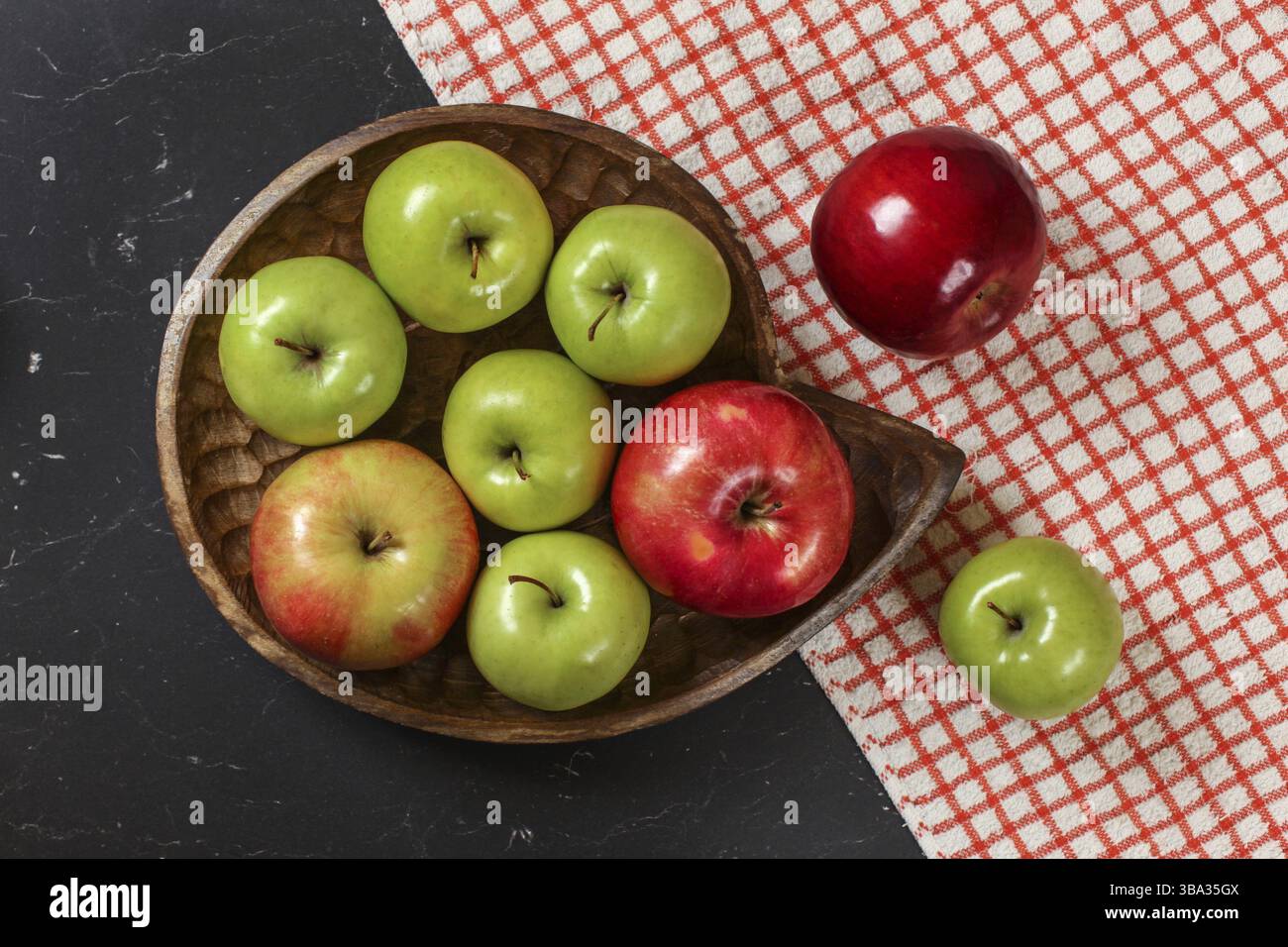 Blick von oben, grün und rot glänzende Äpfel auf hölzernem geschnitzten Schüssel, rote Gingham Tischdecke und dunkle Marmorplatte darunter, Liptovsky Hradok, Slowakei, Europ Stockfoto