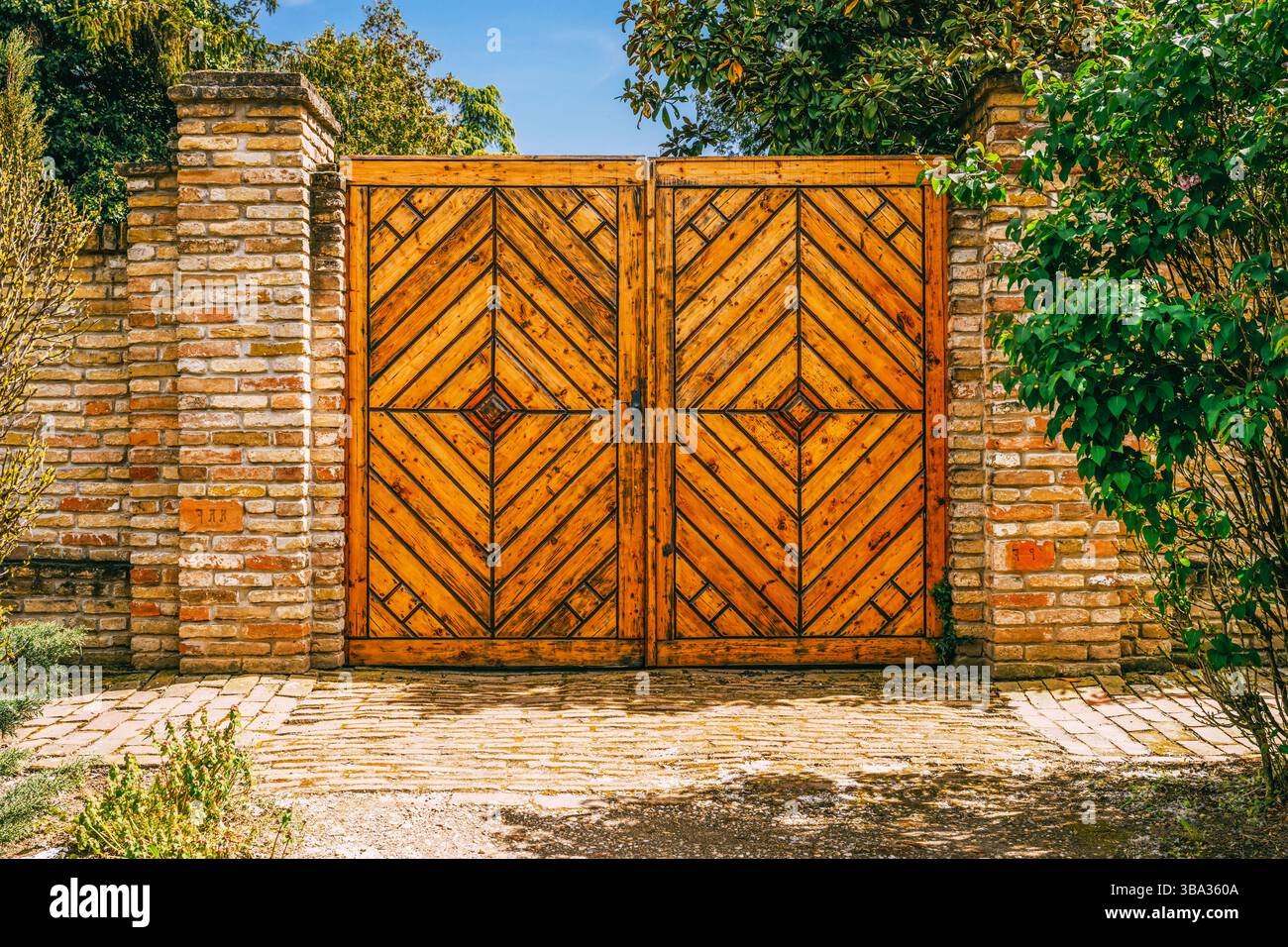 Holztor mit Ziegelsäulen am sonnigen Frühlingstag Stockfoto