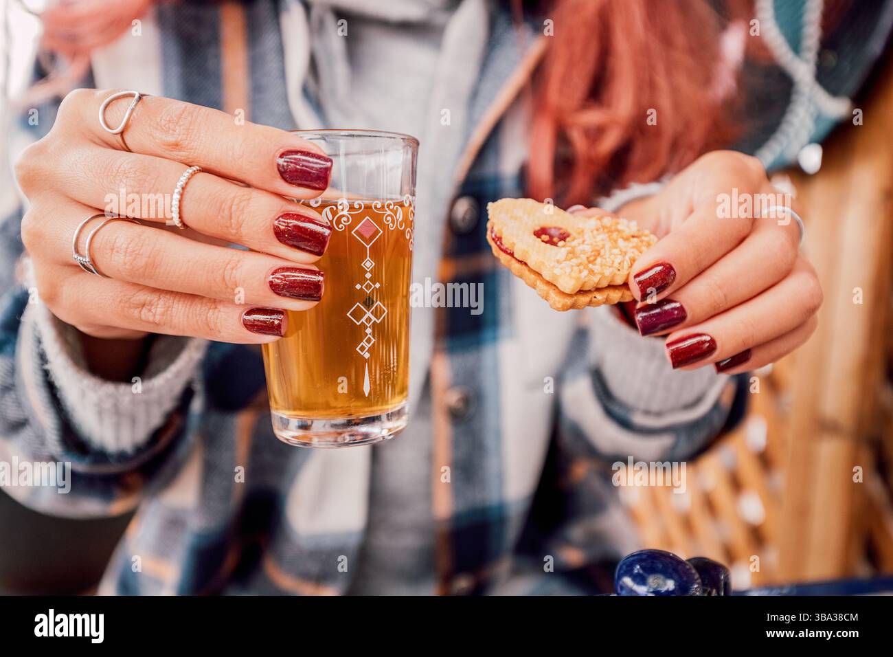 Frau, die während ihres Frühstücks ein dekoriertes Glas marokkanischen Pfefferminztee und einen Keks hält Stockfoto