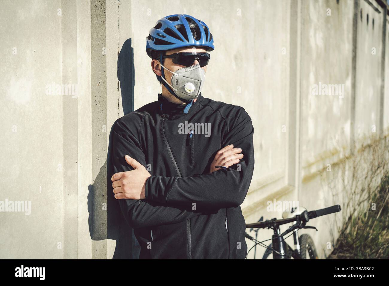 Portrait männlicher Radfahrer in der Nähe grauer Betonwand in Schutzmaske PM 2,5 mit Filter. Schützen Sie menschliche Atemorgane vor Staub und suspendierten PA Stockfoto