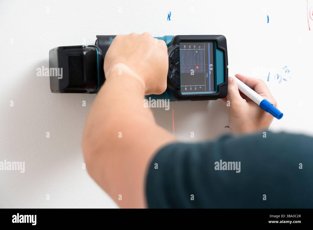 Ein Elektroarbeiter scannt die Wand mit einem digitalen Stiftsucher und markiert erkannte Punkte mit einem blauen Marker. Heimwerkerreparatur, Installationswerkzeuge Stockfoto