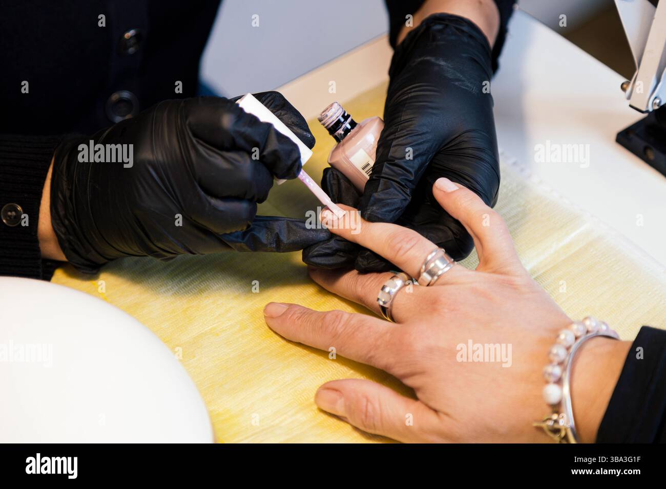 Schönheits- und Nagelsalon. Professionelle Maniküre in schwarzen Handschuhen, nagellack für einen Kunden streichen. Nahaufnahme des Fotos. Stockfoto