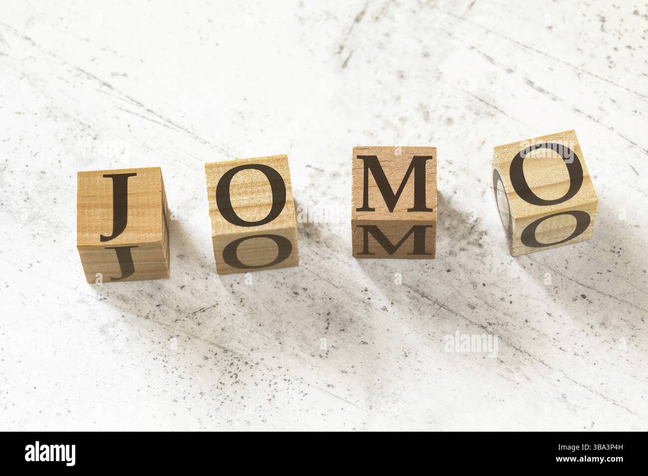 Vier hölzerne Würfel mit den Buchstaben JOMO (was die Freude am Verpassen bedeutet) auf weißem Arbeitsbrett, Liptovsky Hradok, Slowakei, Europa Stockfoto