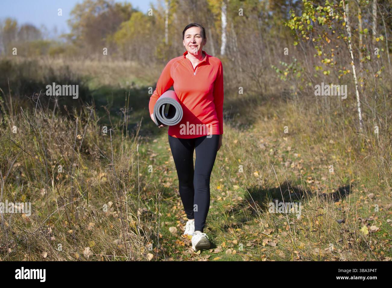 Fröhliche sportliche ältere Frau. Positive Senior Woman hält aufgerollte Trainingsmatte Gesundheit und Sport gehen Hand in Hand. Porträt eines sportlichen älteren Menschen wo Stockfoto