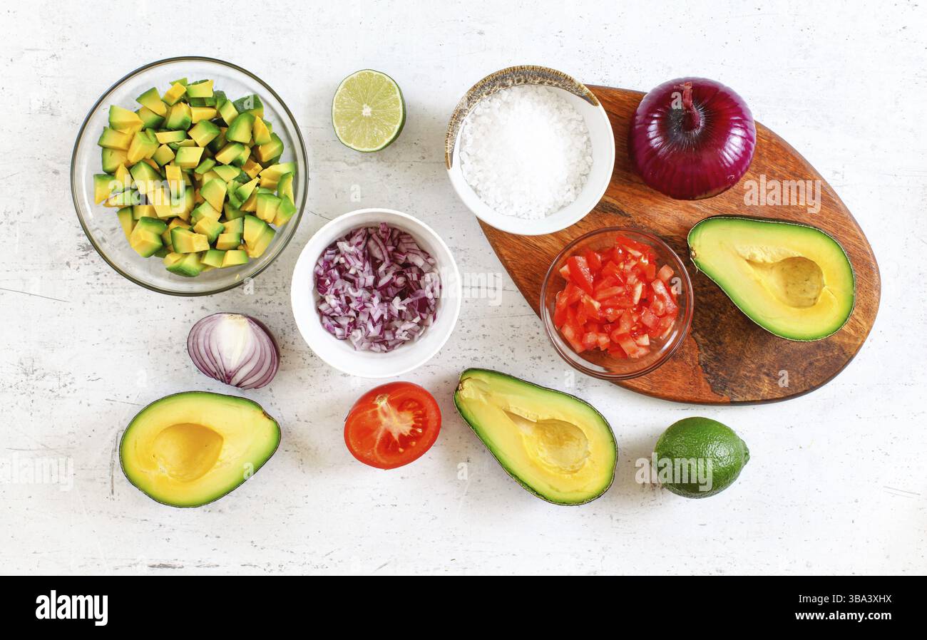Avocadohälften, Stücke, Limetten, Tomaten und Zwiebeln, Tasse mit Salz - grundlegende Guacamole Zutaten auf weißem Arbeitsbrett, Flachbild-Foto, Liptovsky Hradok Stockfoto