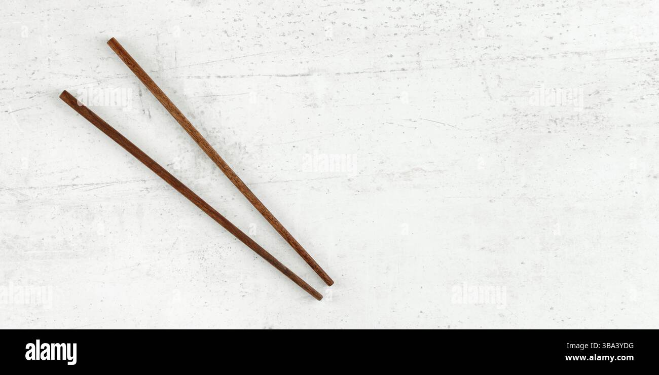 Flaches Foto – zwei Essstäbchen aus dunklem Holz auf Weißtafel. Breites Banner für asiatische/chinesische Speisen, Platz für Text rechts, Liptovsky Hradok, Slovaki Stockfoto
