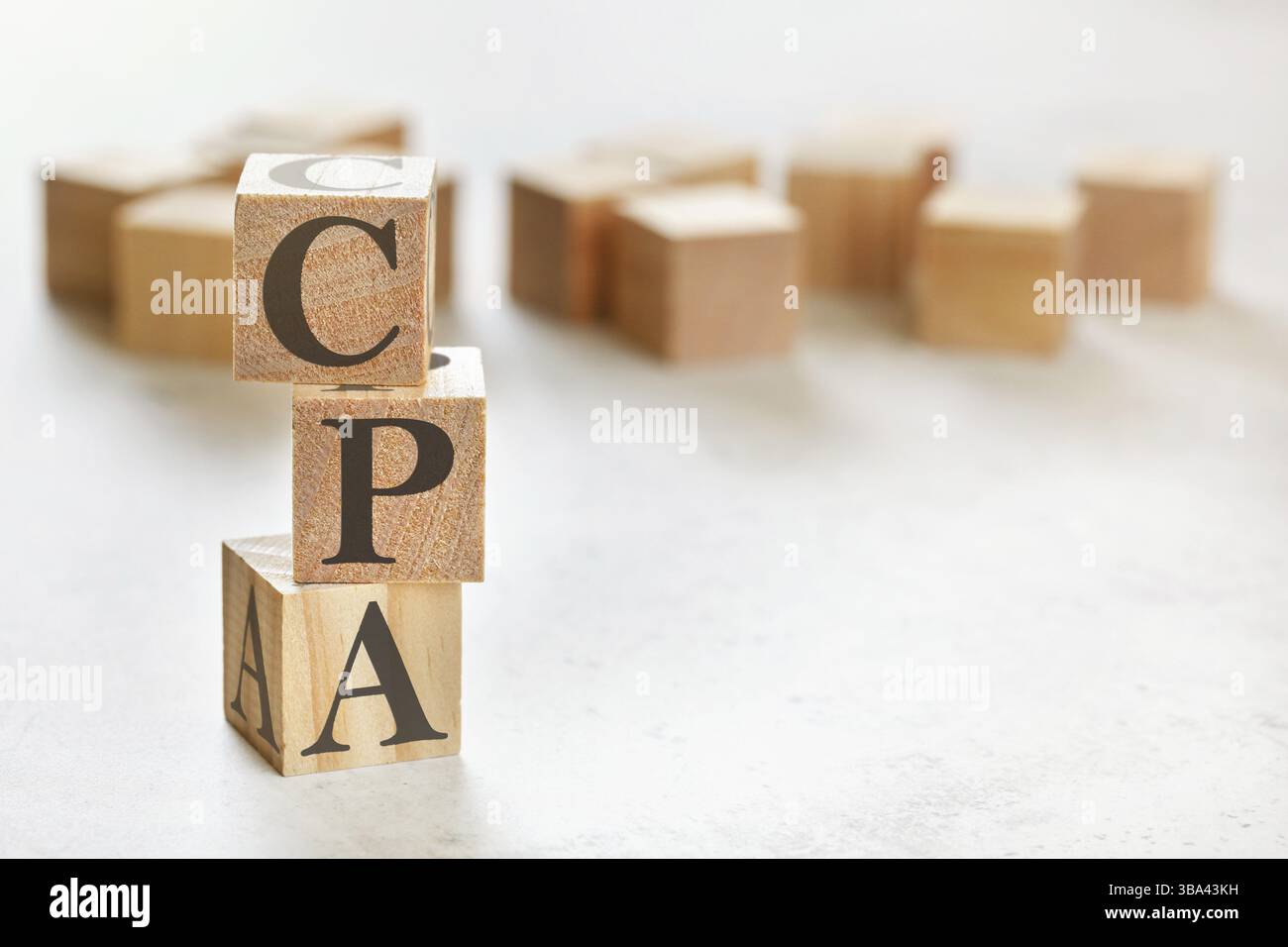 Drei Holzwürfel mit den Buchstaben CPA (bedeutet Kosten pro Aktion/Akquisition), auf weißem Tisch, mehr im Hintergrund, Platz für Text in der rechten unteren Ecke, Li Stockfoto