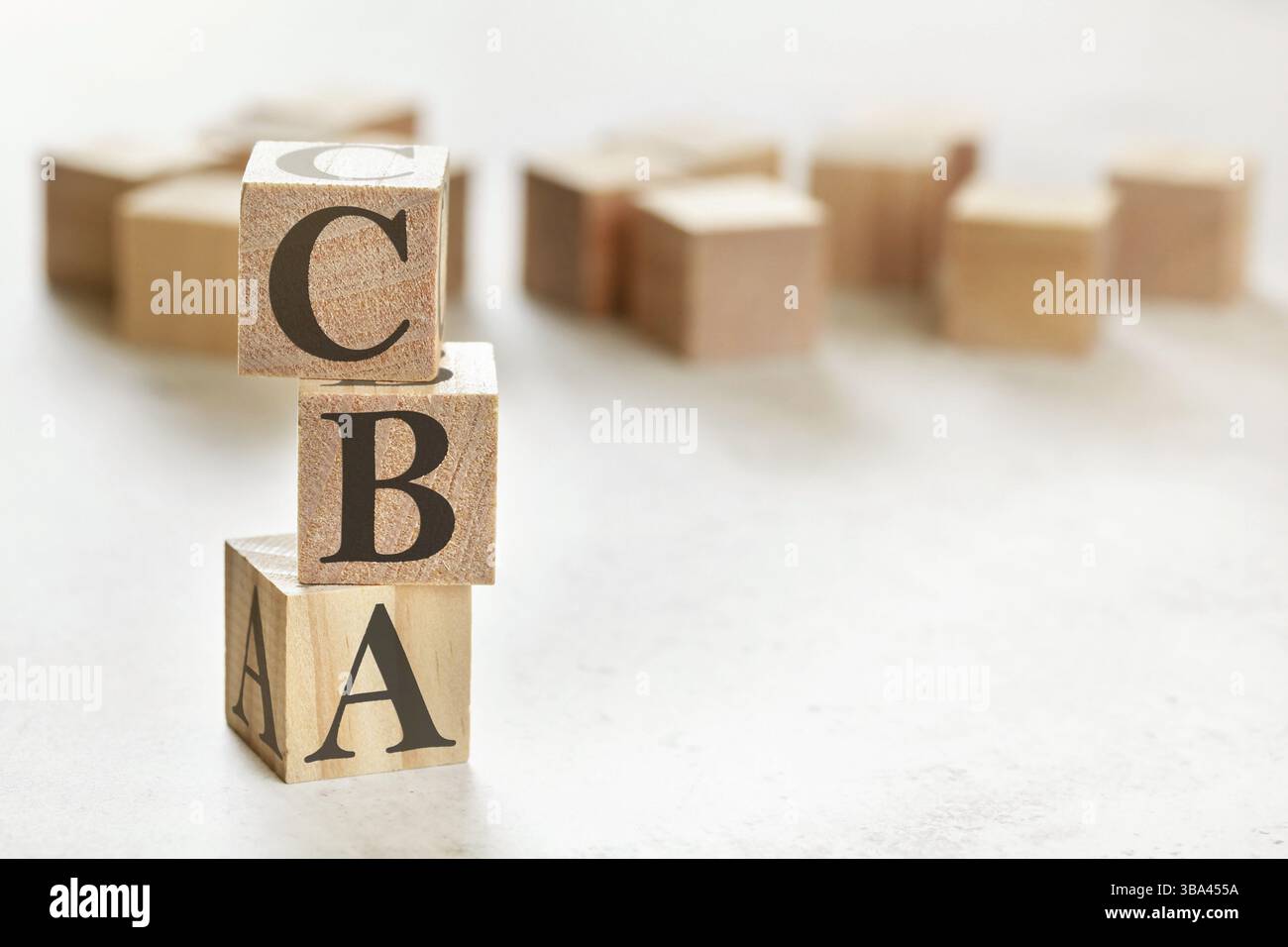 Drei hölzerne Würfel mit den Buchstaben CBA (bedeutet Kosten-Nutzen-Bewertung), auf weißem Tisch, mehr im Hintergrund, Platz für Text in der rechten unteren Ecke, Liptovsk Stockfoto