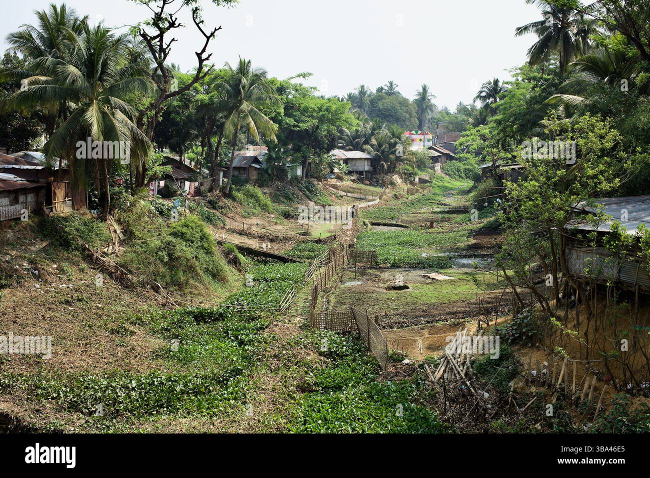 Stelzenhäuser und Existenzgrundstücke entlang einer Trockenwasserstraße in Rangamati, Bangladesch, offenbaren den Druck von Landknappheit und saisonaler Dürre. Stockfoto