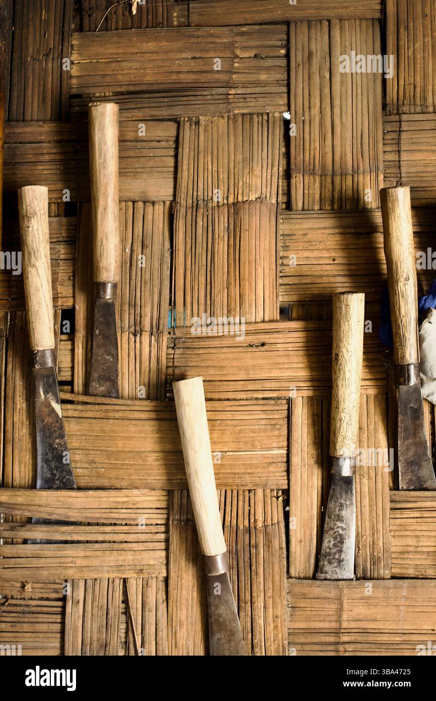 Lokal hergestellte Messer mit Holzgriffen hängen an einer Wand aus gewebtem Bambus in einer Tripura-Stammeshütte in der Nähe von Bandarban im Südosten Bangladeschs. Stockfoto
