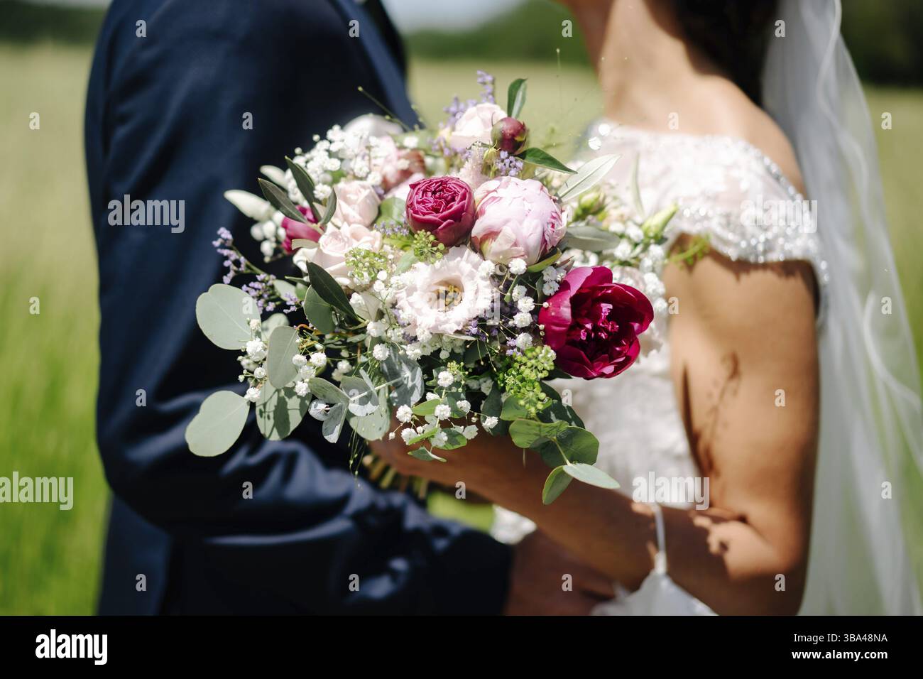 Foto einer Braut mit Blumenstrauß und dem Bräutigam im Garten Stockfoto