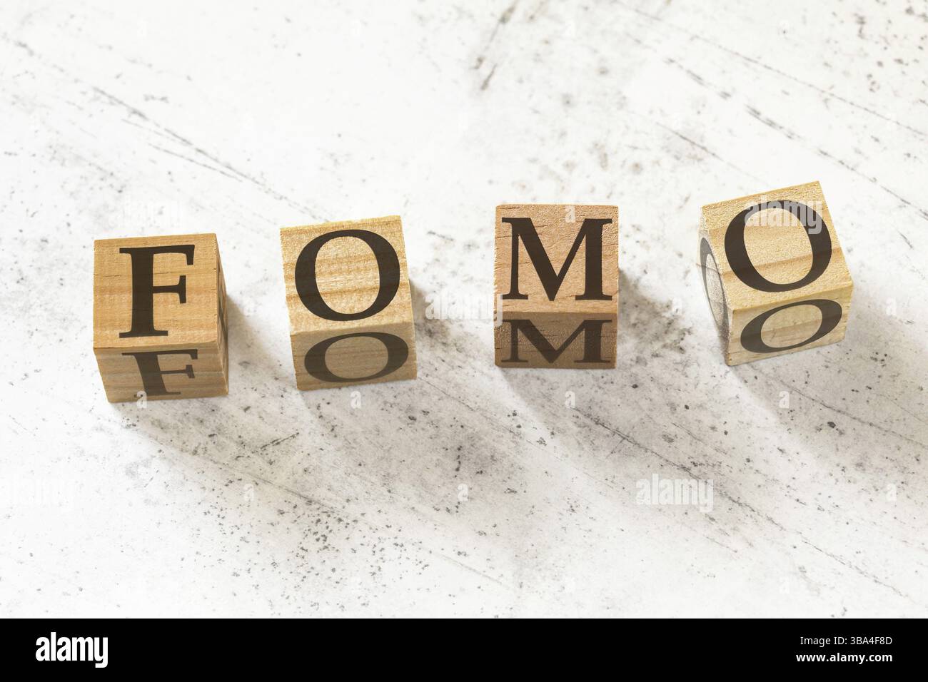 Vier hölzerne Würfel mit den Buchstaben FOMO (was Angst vor dem Verpassen bedeutet) auf weißem Arbeitsbrett, Liptovsky Hradok, Slowakei, Europa Stockfoto