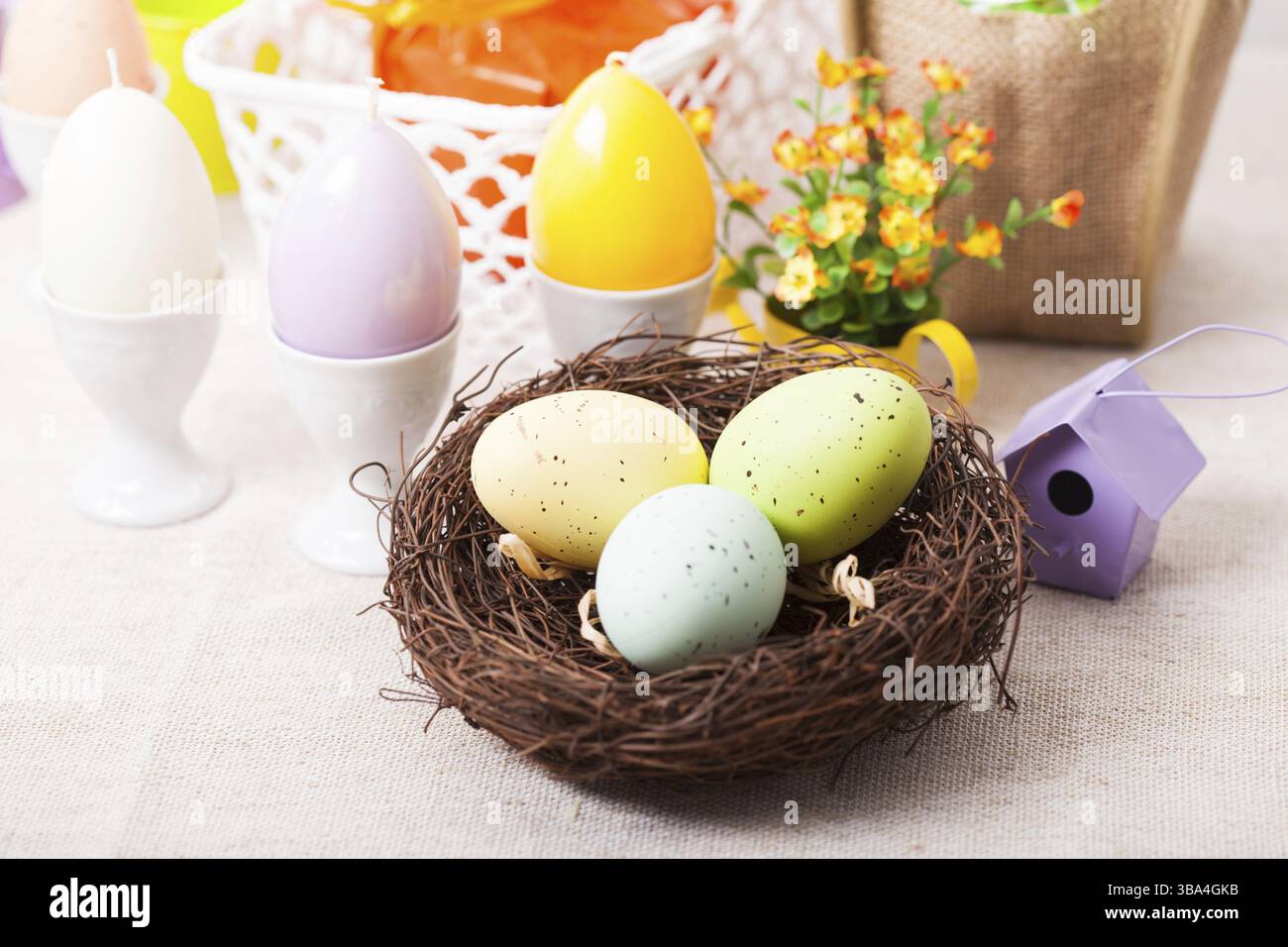 Osterdekorationen - Eierkerzen, Nest und Blumen auf dem Tisch Stockfoto