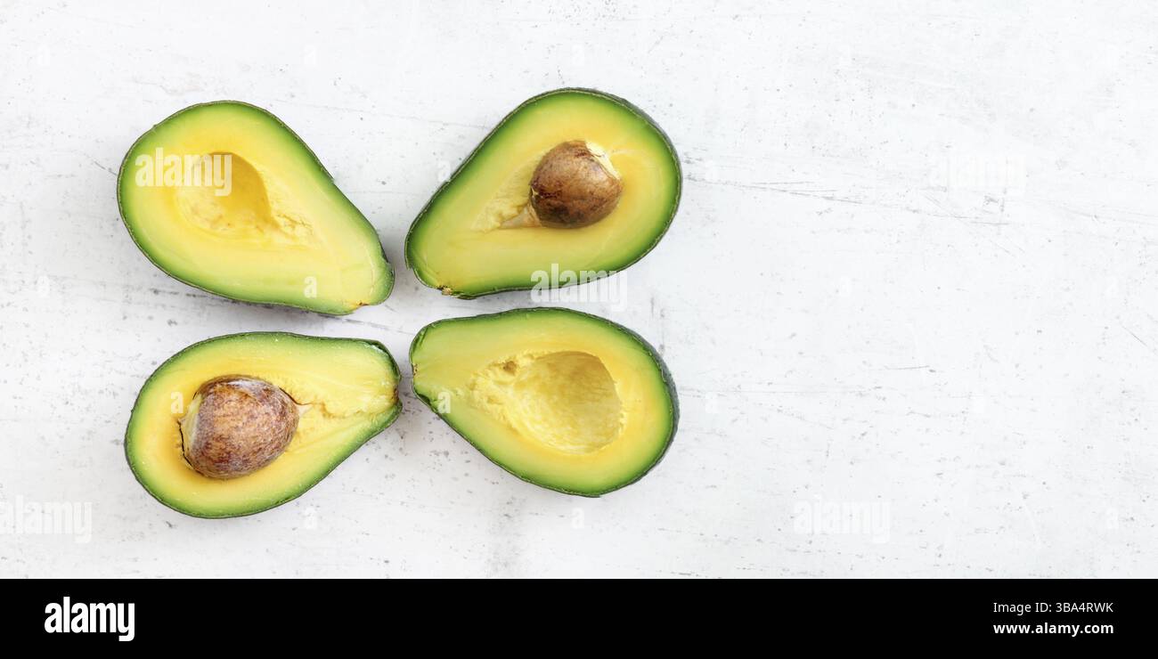 Kopfaufnahme - vier Avocadohälften, zwei mit sichtbarem Samen, auf weißem Arbeitsbrett, breiter Bannerraum für Text auf der rechten Seite, Liptovsky Hradok, Slowakisch Stockfoto