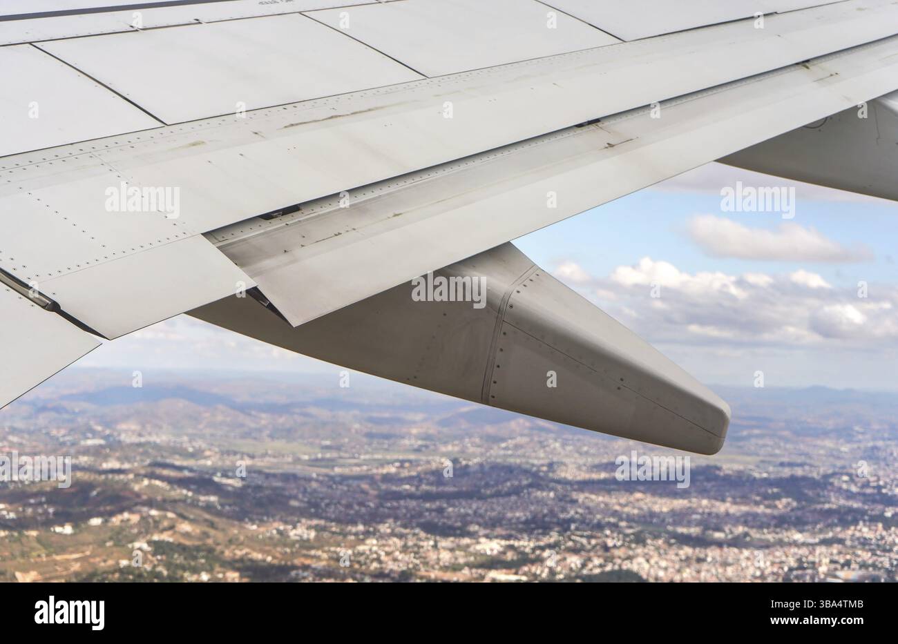 Blick vom Passagierfenster aus auf das kommerzielle Flugzeug, verschwommene Stadtlandschaft sichtbar unter dem Flugzeugflügel, Antananarivo, Madagaskar, Afrika Stockfoto