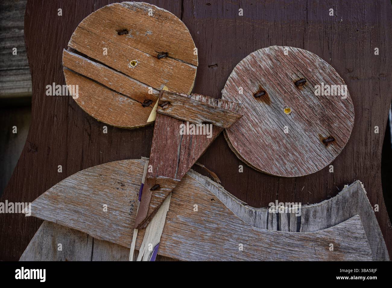 Schäbige braune Eulendekoration mit Holzausschnitten hängt an einem Holzzaun. Die Dekoration fällt auseinander, alt und zersplittert, mit abblätternder Farbe. Stockfoto