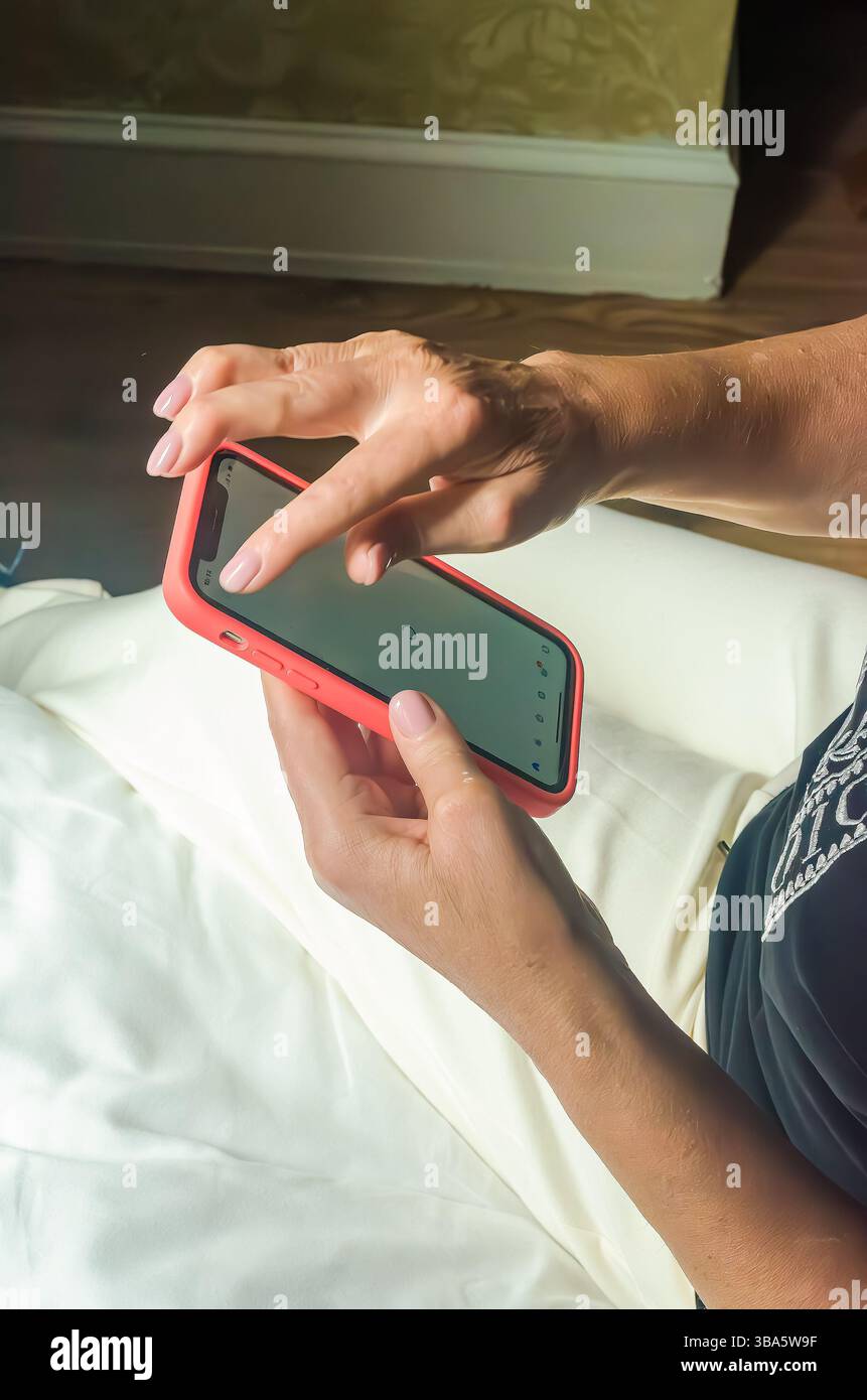 Hände interagieren mit dem Smartphone auf einer weichen Oberfläche in warmen Innenräumen mit natürlichem Licht. Hochwertige Fotos Stockfoto