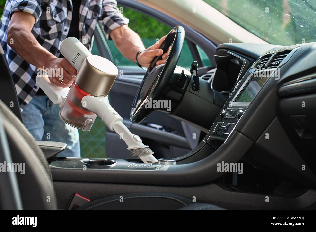 Man verwendet einen Handstaubsauger, um die Mittelkonsole des Fahrzeuginnenraums zu reinigen. Moderne Innenraumreinigung und -Wartung Stockfoto