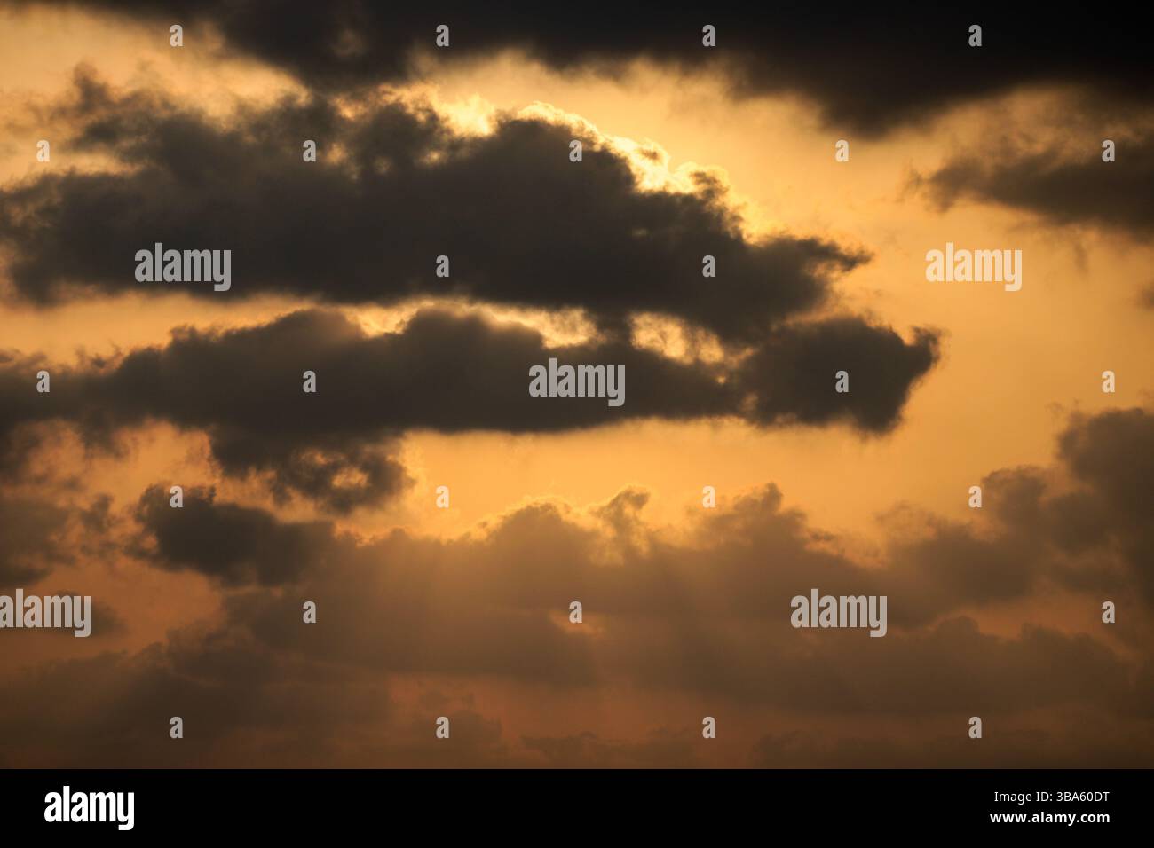 Goldener Sonnenuntergangshimmel mit dramatischen dunklen Wolken und Sonnenstrahlen, die durch eine atemberaubende Naturszene strömen. Stockfoto