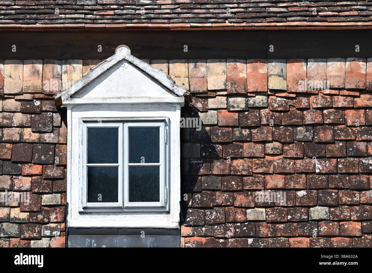 Vintage-weißes Dachfenster auf verwittertem rustikalem Terrakotta-Fliesendach Stockfoto