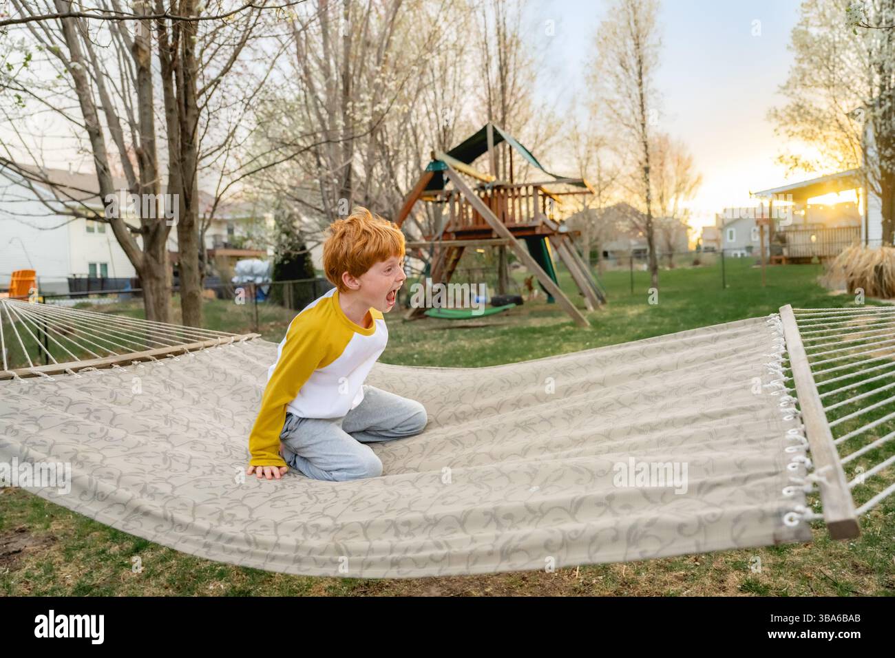 Junge mit großem Lächeln, der im Frühling in der Hängematte im Garten spielt Stockfoto