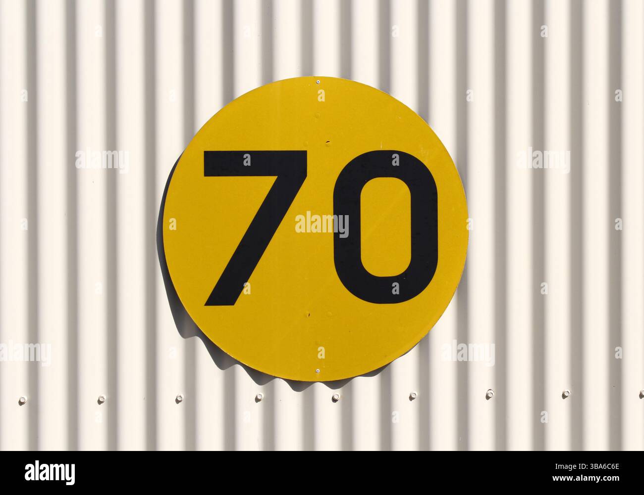 Rundes gelbes Schild mit der Nummer 70 in Schwarz, montiert auf einer gewellten Metallwand Stockfoto