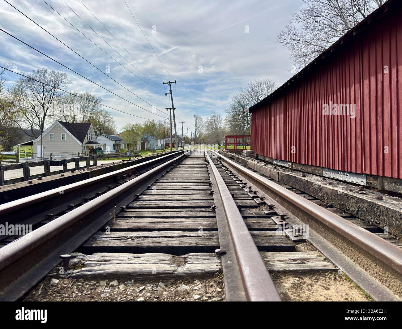 Eisenbahngleise neben der roten überdachten Brücke, die durch eine kleine Stadt führt Stockfoto