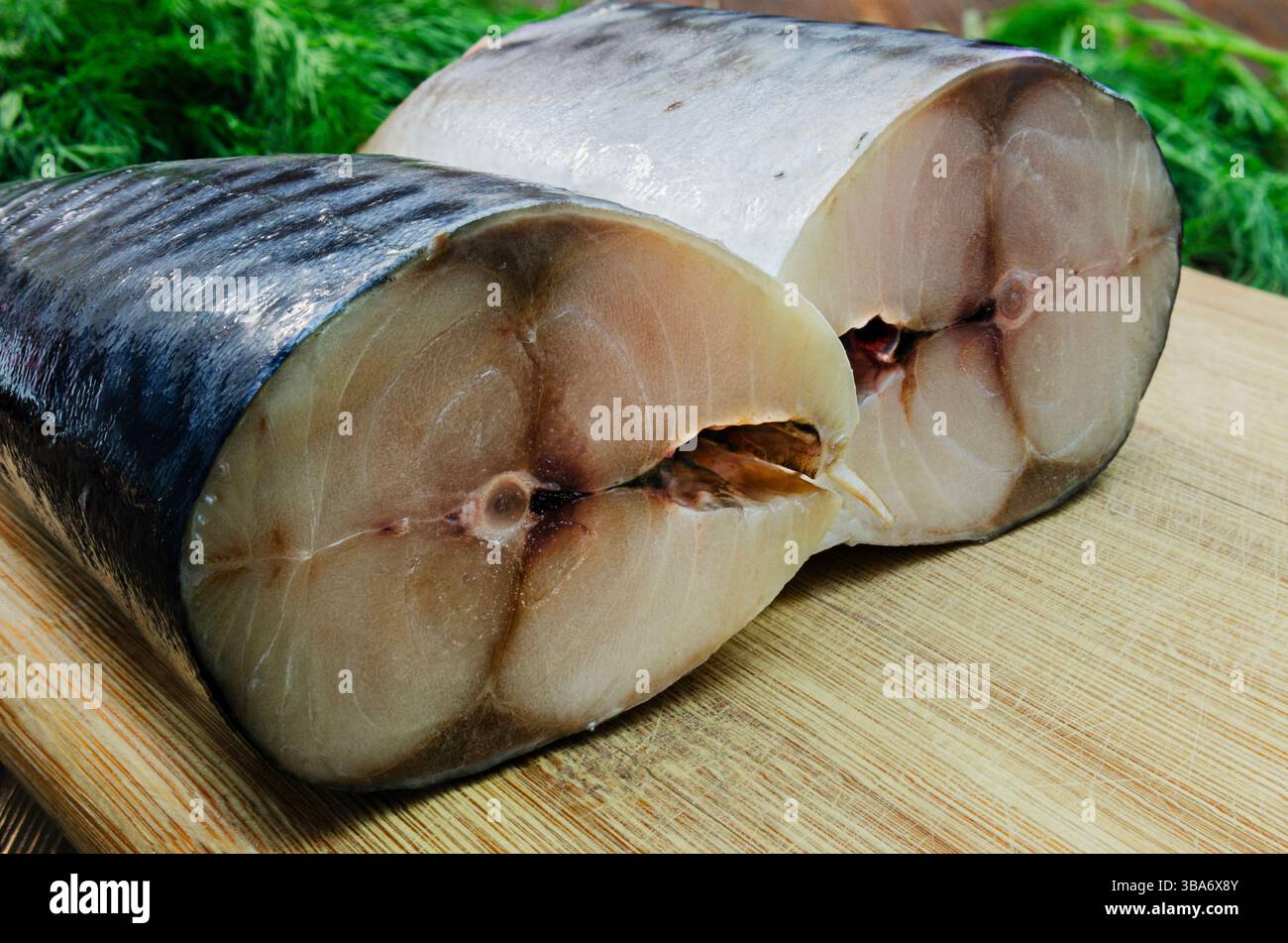 Nahaufnahme von frisch geschnittenen Makrelenscheiben auf einem Holzschneidebrett, die die glänzende Haut und das zarte Fleisch des Fisches zeigen. Stockfoto