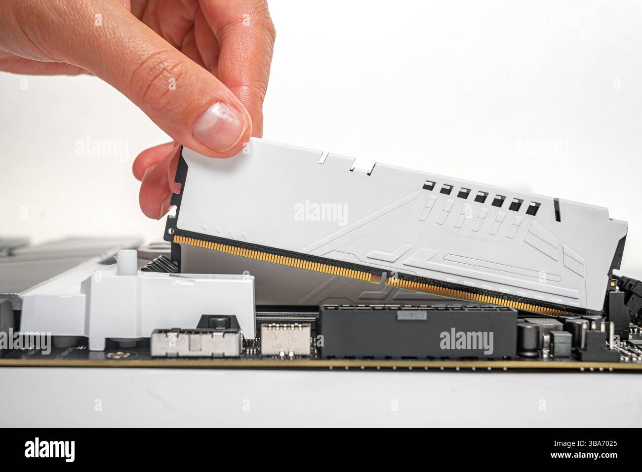 Eine Person setzt vorsichtig ein weißes DDR-RAM-Modul in einen Hauptplatinensteckplatz ein Stockfoto