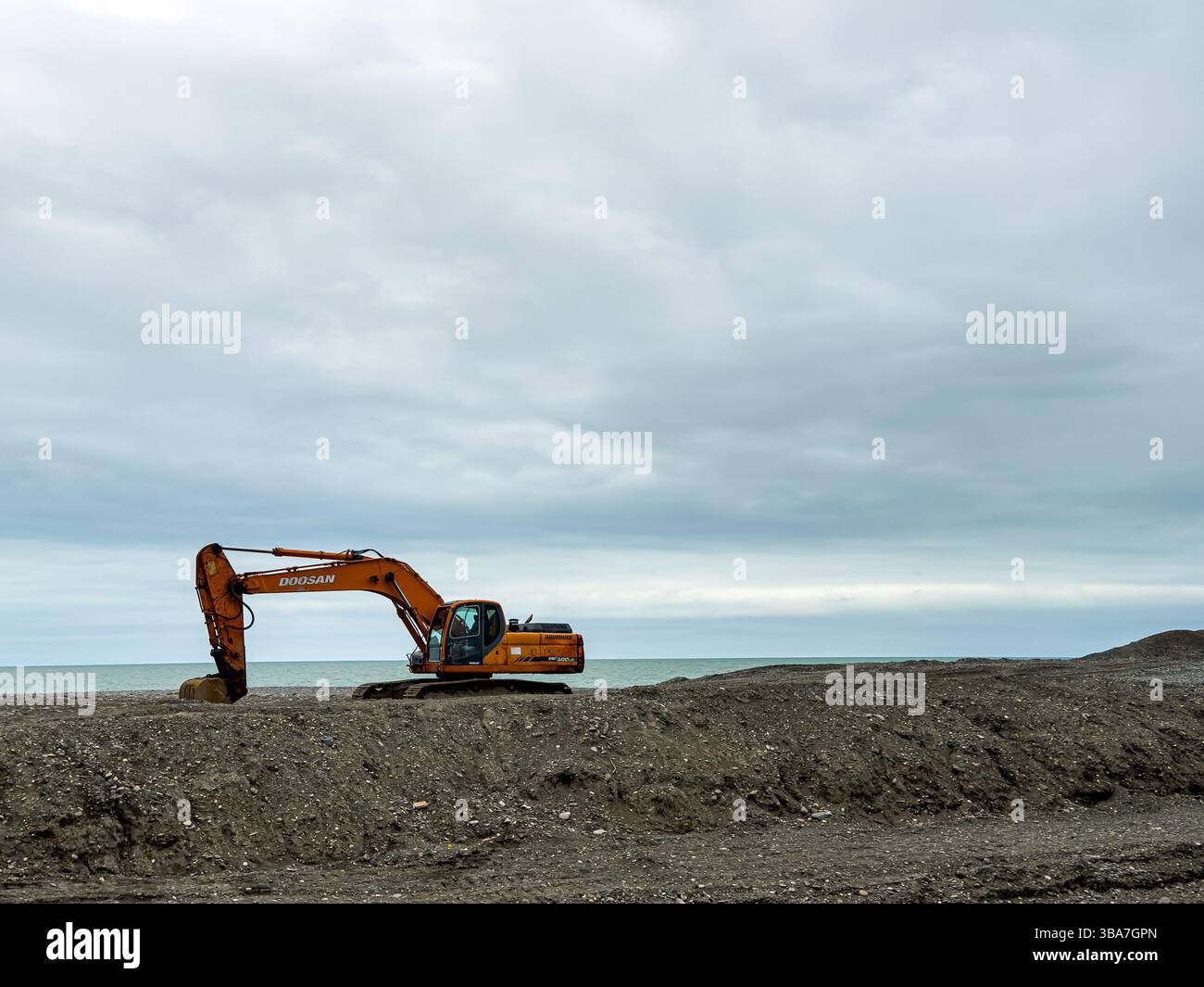 Bagger auf der Baustelle an der Küste unter bewölktem Himmel, Weitblick, keine Leute. Industrie-, Infrastruktur- und Landentwicklungskonzept. Stockfoto