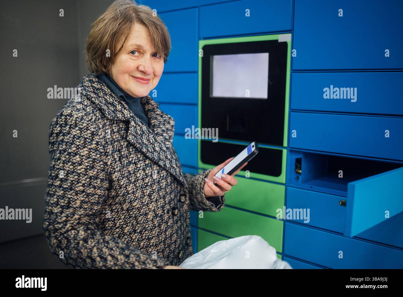 Eine ältere Frau tippt auf das Display, um ein Paket zu erhalten. Eine reife Dame in lässiger Kleidung gibt Daten auf einem Paketautomaten ein. Der Rentner hält das Telefon Stockfoto