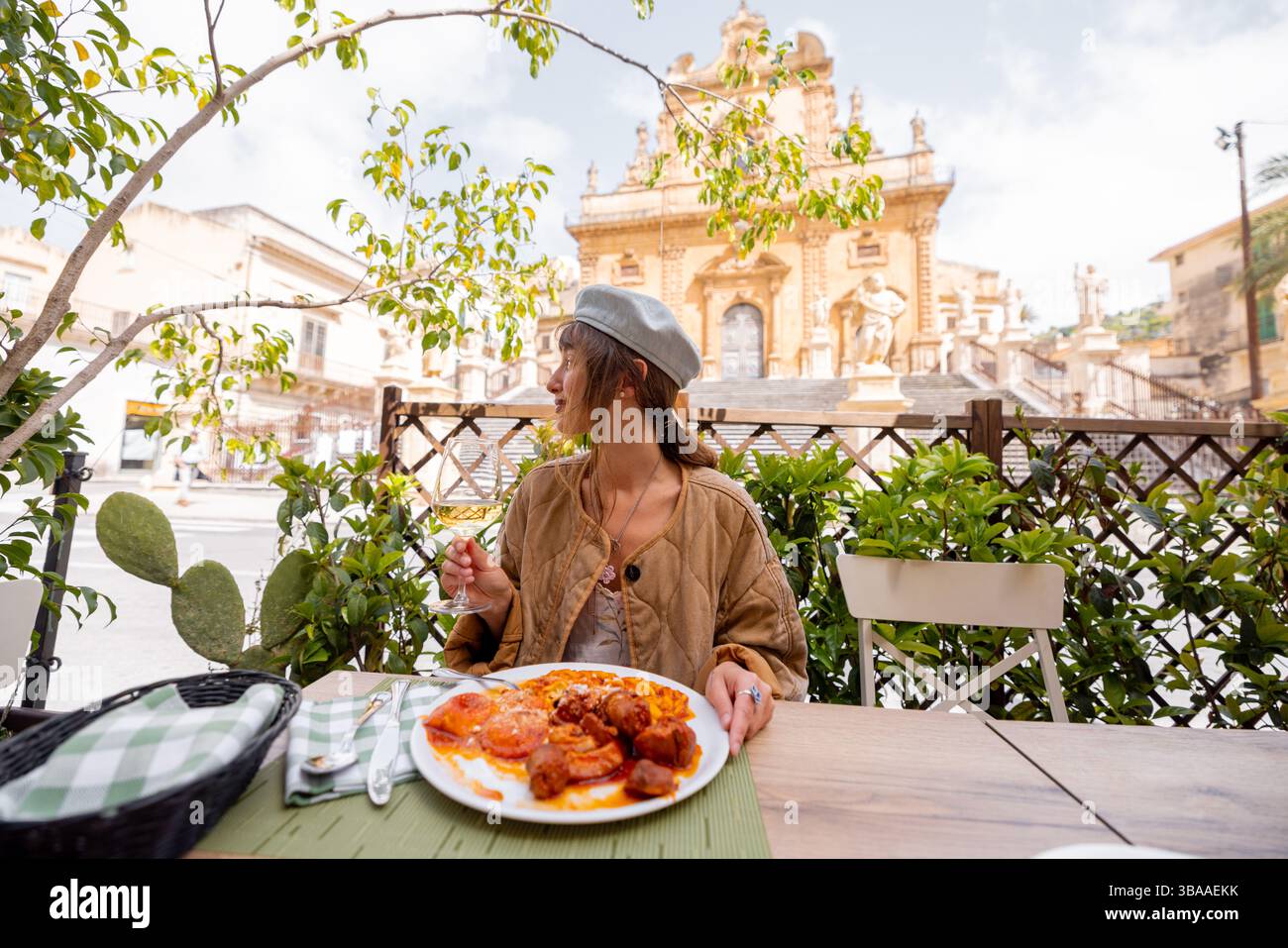 Die lächelnde Frau genießt ein herzhaftes sizilianisches Mittagessen mit Gnocchi, Fleischbällchen und Tomatensoße, gepaart mit Weißwein, in einem Restaurant im Freien vor der Petersdom in Modica Stockfoto