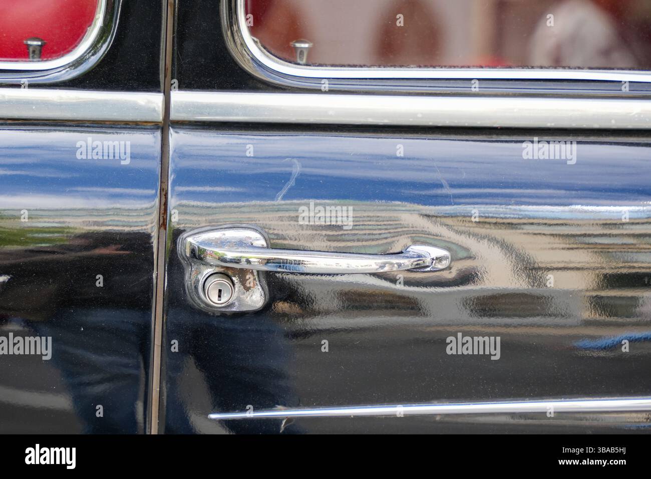 Nahaufnahme des verchromten Türgriffs eines schwarzen Oldtimers. Detailansicht eines Türgriffs und Schlosses aus poliertem Chrom bei einem Hochglanz-Oldtimer in Schwarz, mit R Stockfoto