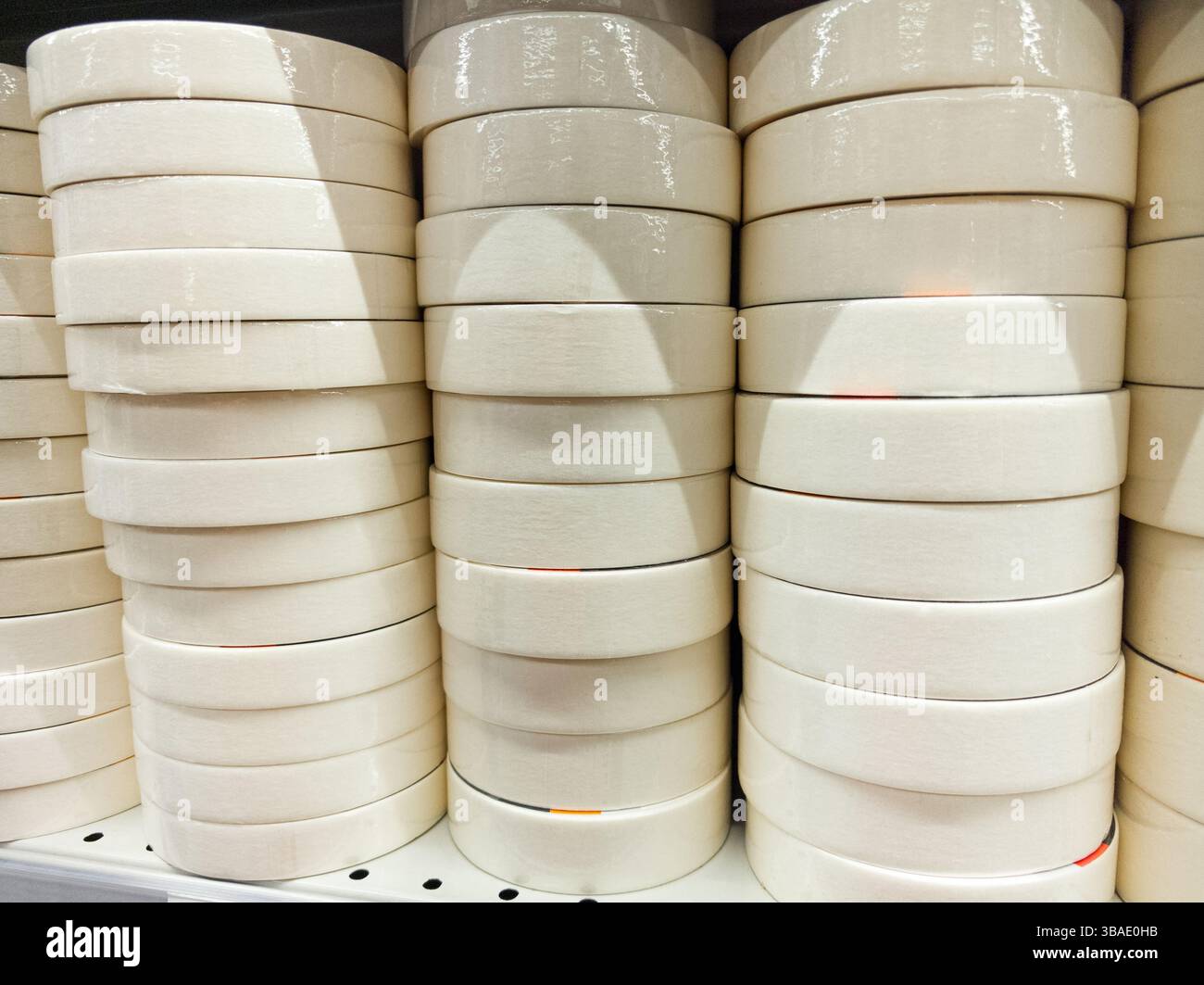 Eine Sammlung sauberer, weißer Klebebandrollen ist ordentlich in einem Verkaufsregal angeordnet. Die Rollen weisen eine einheitliche Form auf, wodurch sie optisch ansprechend wirken Stockfoto