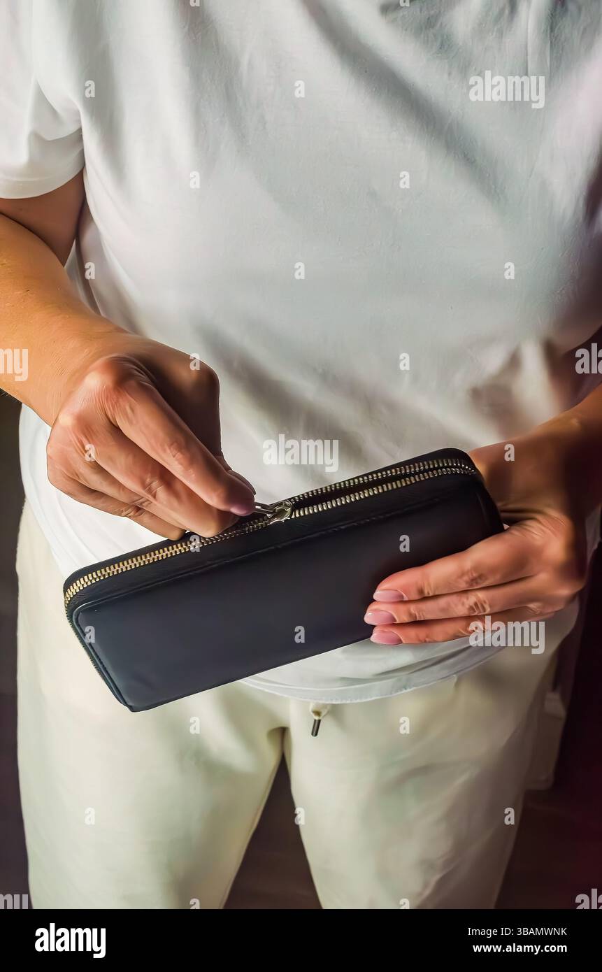 Die weibliche Figur hält eine schwarze Brieftasche und bereitet sich darauf vor, sie in einem gemütlichen Innenraum zu öffnen. Hochwertige Fotos Stockfoto