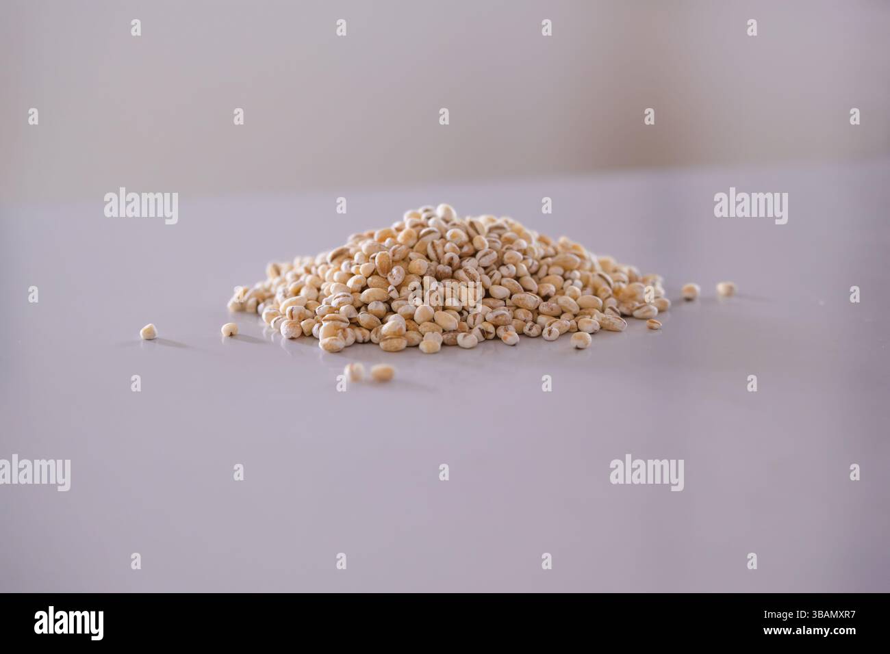 Eine Nahaufnahme eines kleinen Hügels von hellen, ovalen Perlgerstenkörnern auf einer glatten, hellen Oberfläche. Stockfoto