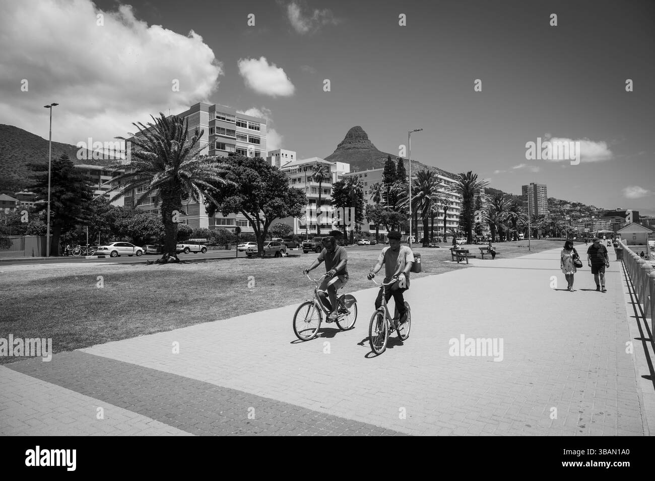 Die Menschen radeln und fahren mit dem Fahrrad entlang der Strandmauer im Stadtteil Sea Point. Kapstadt, Südafrika. Stockfoto